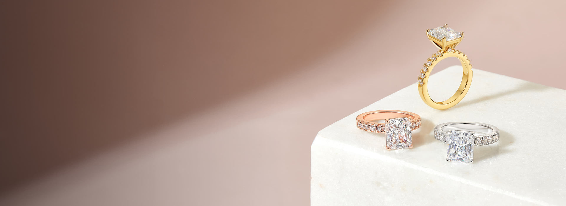 flatlay with gold, rose gold, and silver radiant cut engagement rings with soft pink background