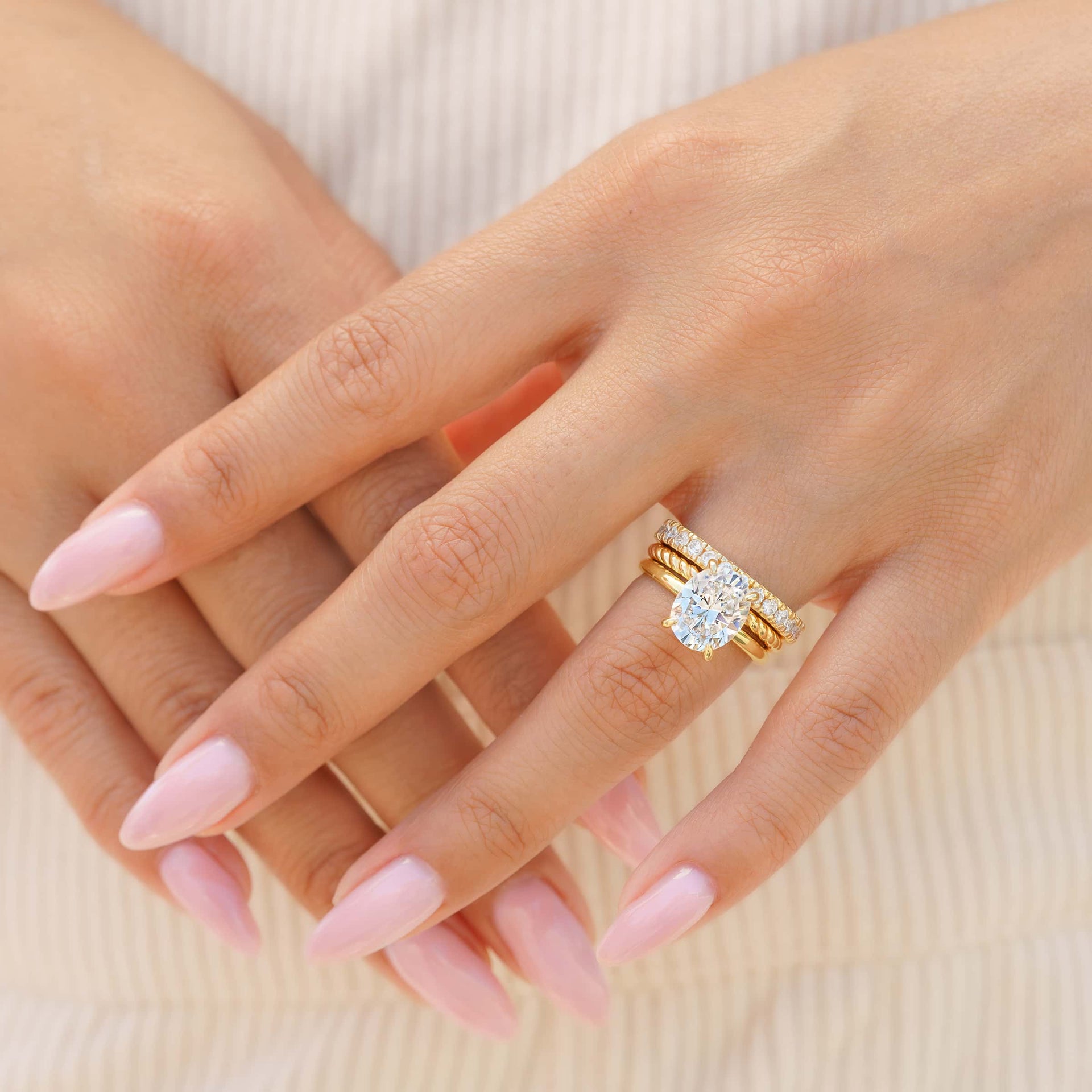 woman wearing gold oval shaped engagement ring with triple stack of wedding bands
