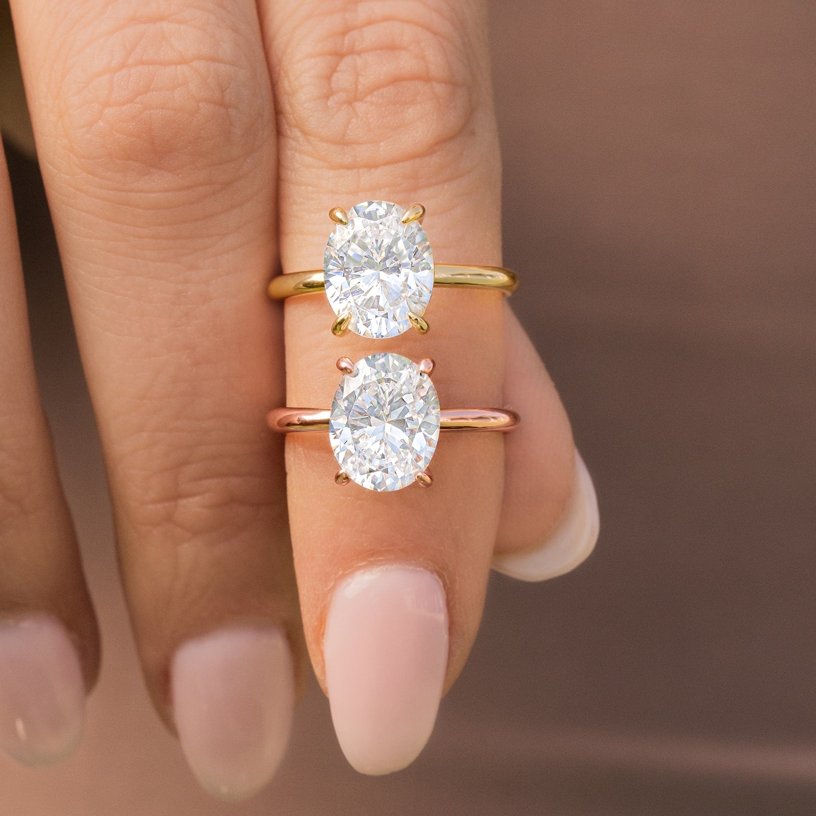woman pinching gold and rose gold oval engagement rings