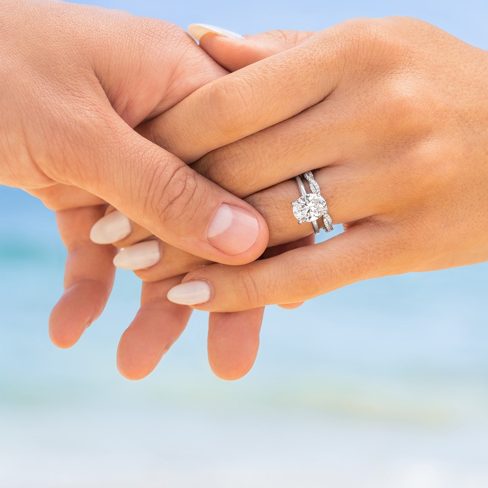 couple holding hands wearing oval cut silver engagement ring