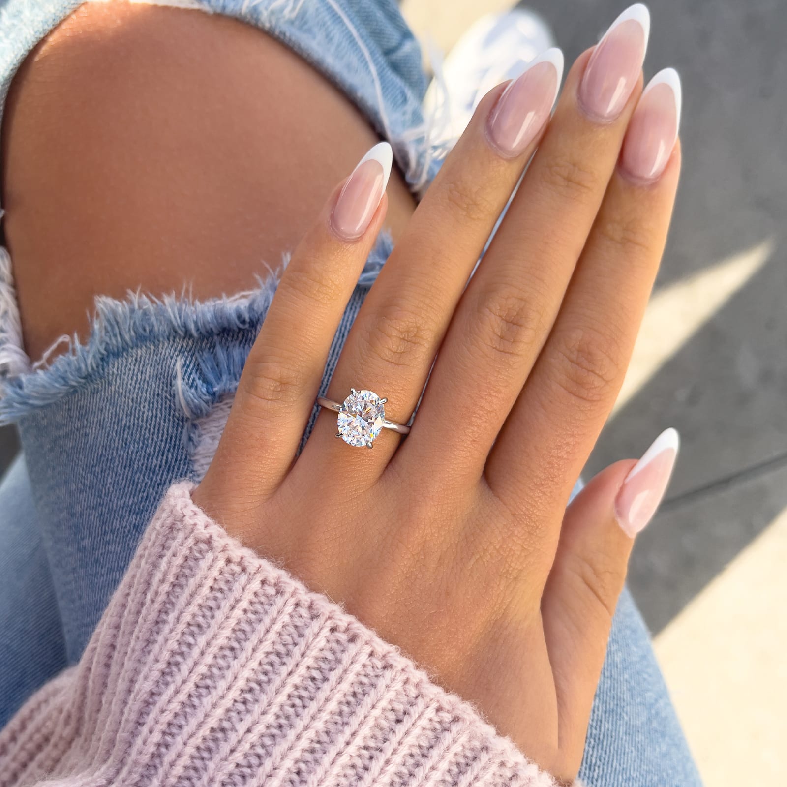 woman wearing silver oval cut engagement ring by jeans