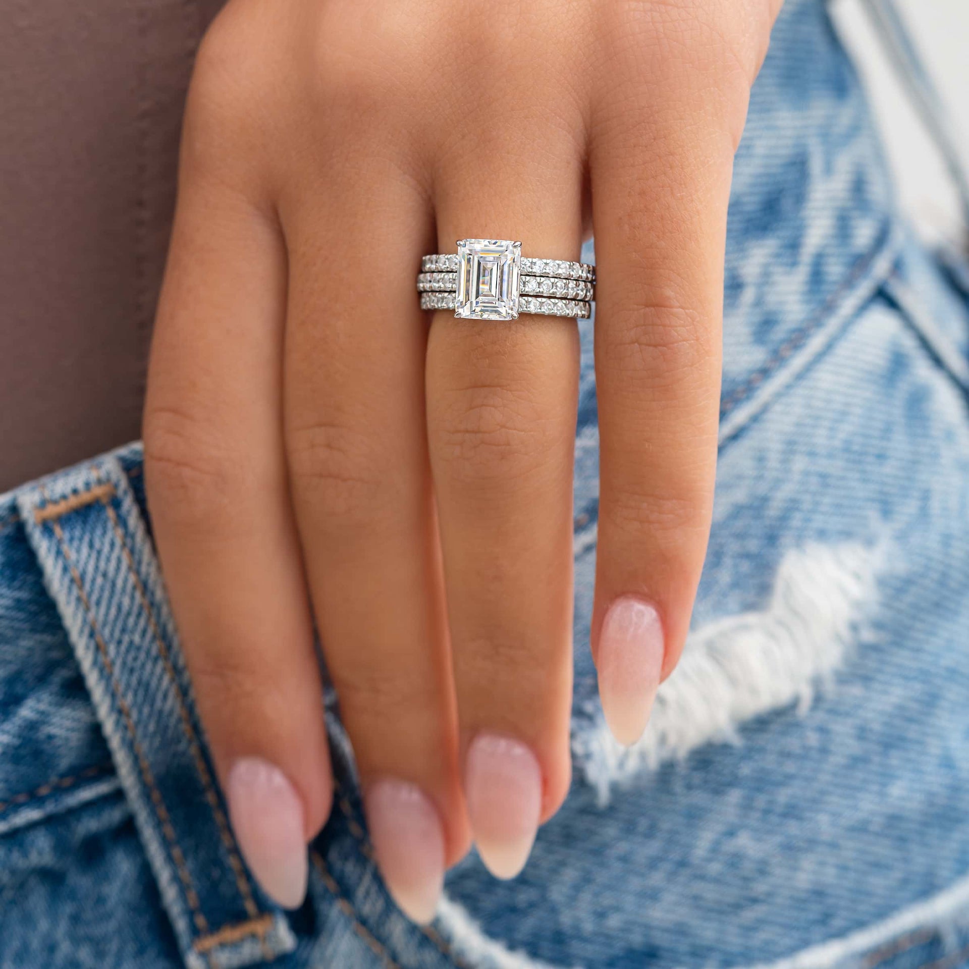 silver 3 carat emerald cut engagement ring stacked with two wedding bands on both sides modeled on female hand