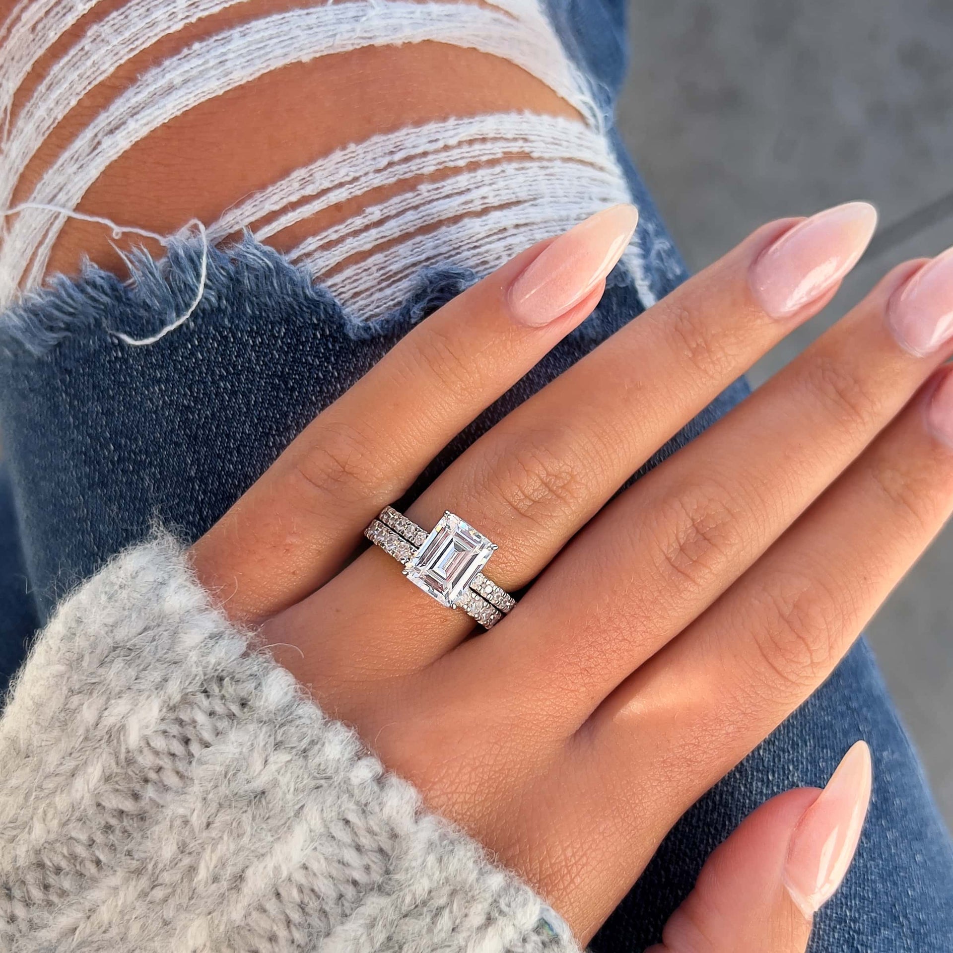 stunning 3 carat emerald cut engagement ring paired with wedding band on female hand resting on blue jeans
