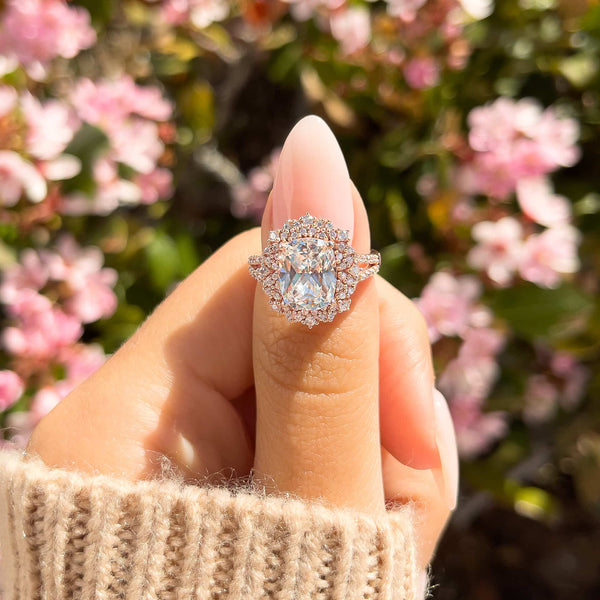 woman pinching rose gold sol engagement ring on finger with brown sweater and pink flowers in background