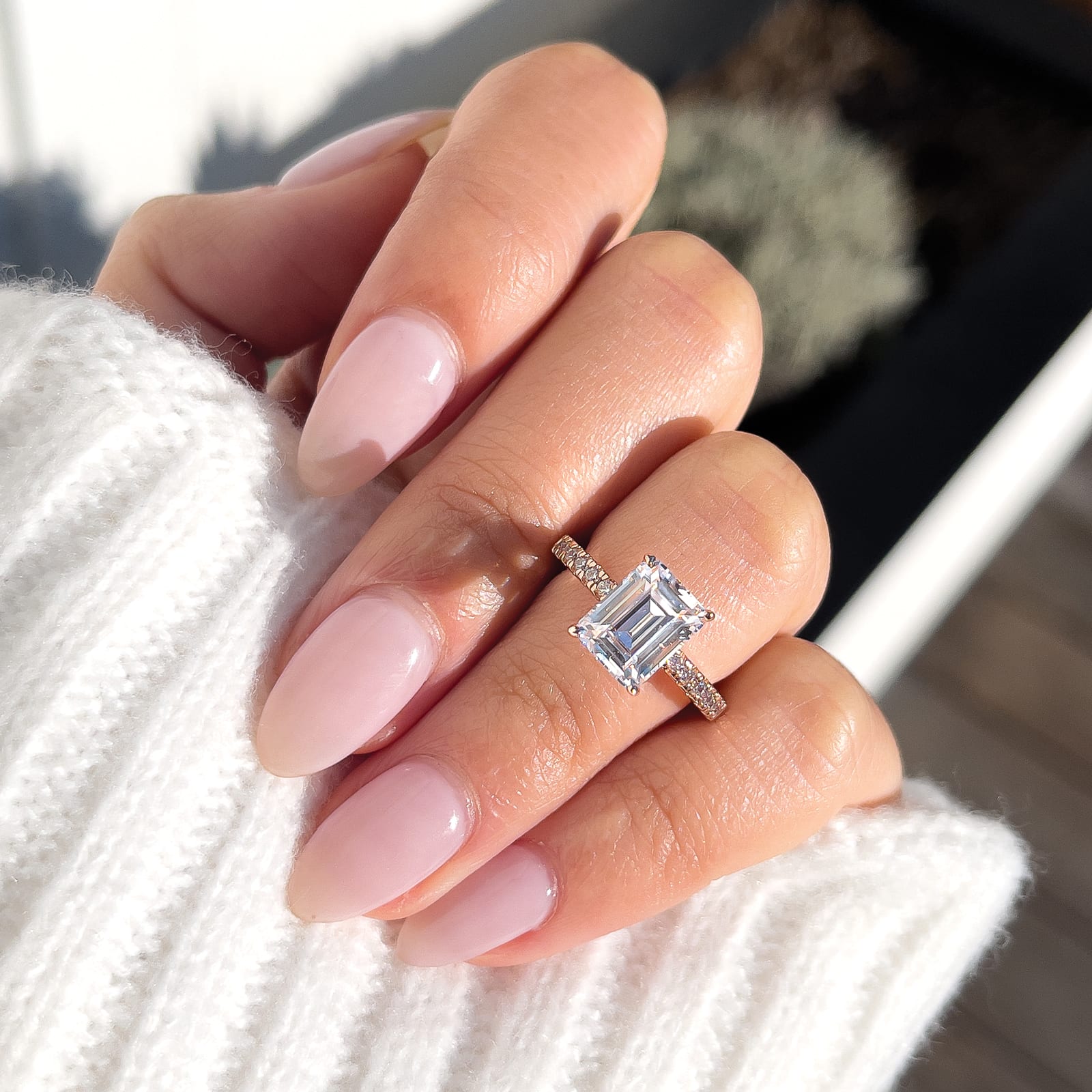 woman pinching rose gold emerald cut engagement ring with white sweater