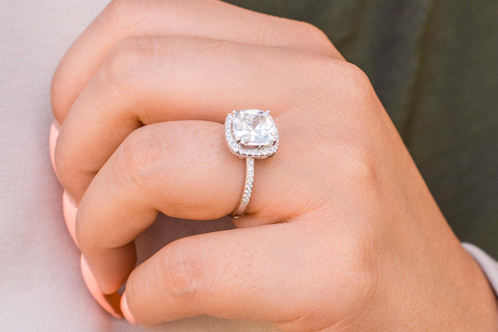 a close up of a womans hand wearing a cushion cut engagement ring