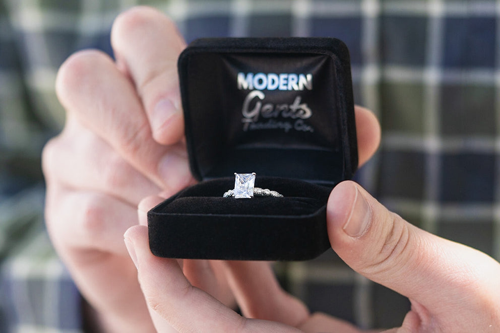 a person holding open a modern gents ring box with an engagement ring inside