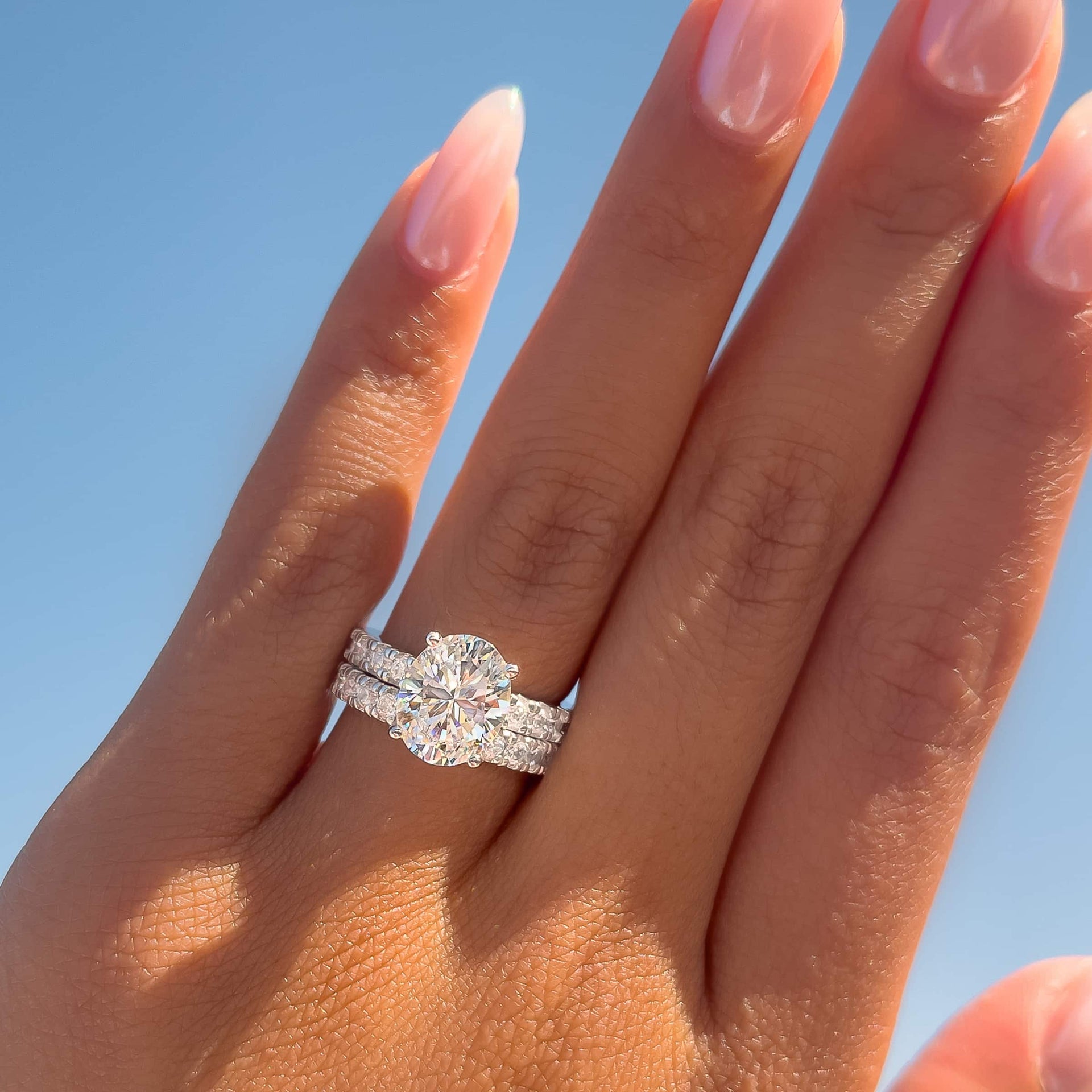 gorgeous oval cut silver engagement ring and matching wedding band on model with neutral nails