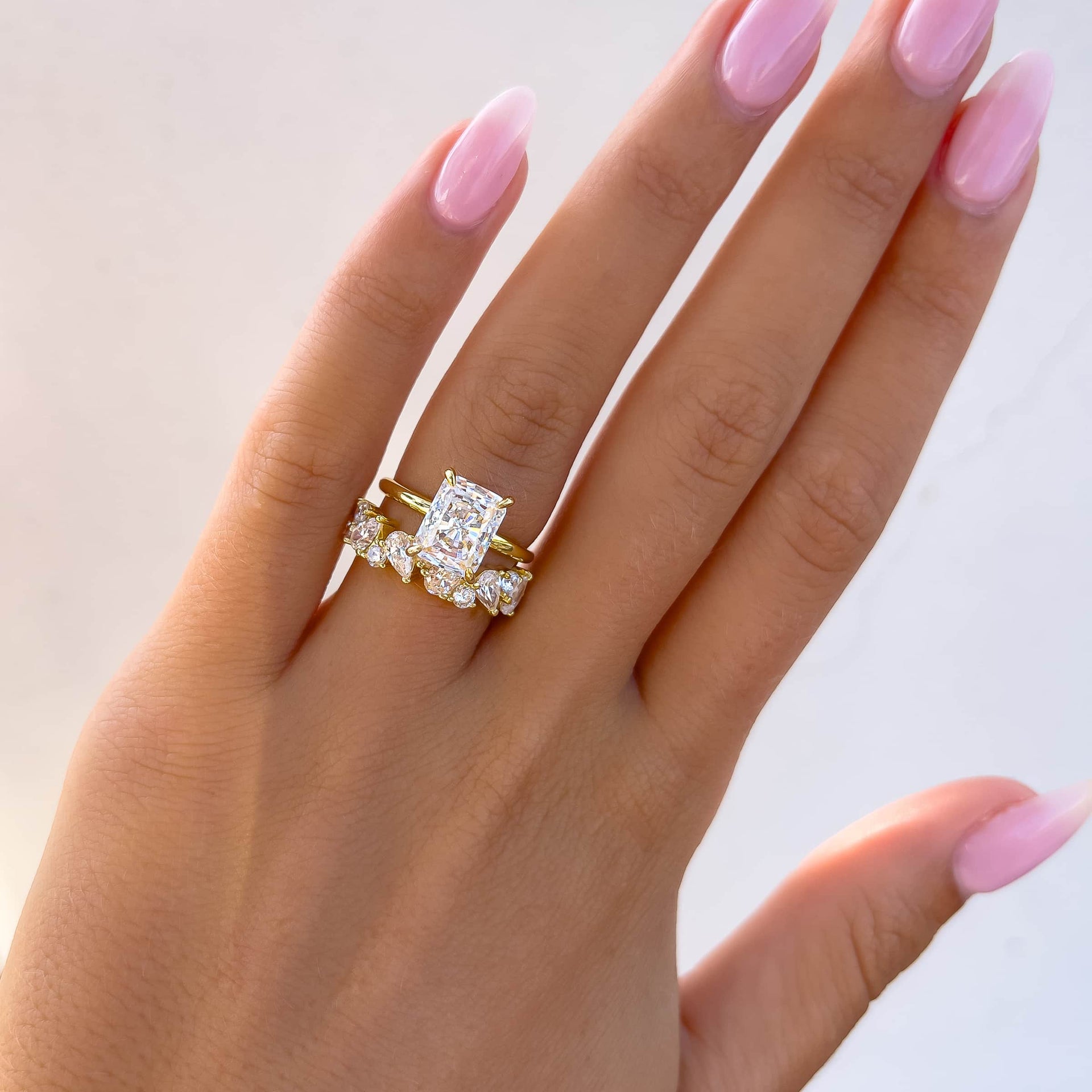 simple, yet bold gold wedding ring set made of a 3 carat radiant cut solitaire engagement ring and a multi-cut statement wedding band on model with light pink nails