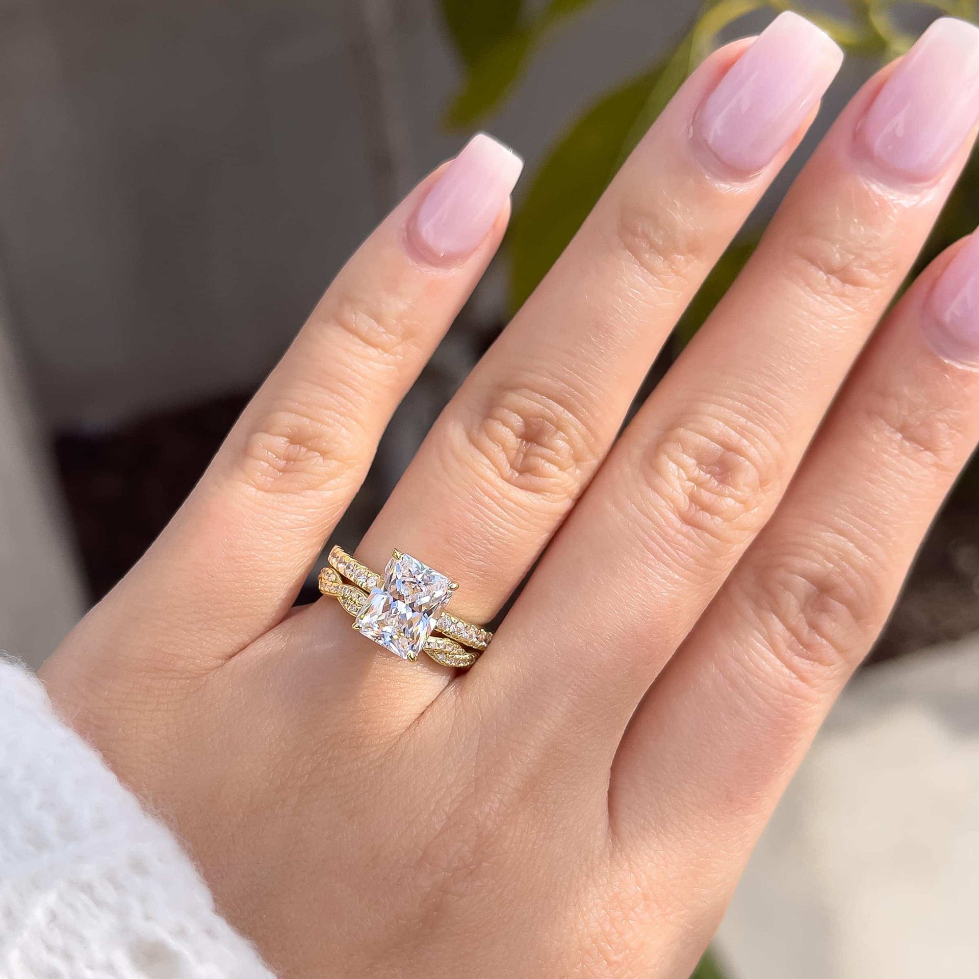3 carat engagement ring shown in gold paired with a vintage twisting detail band shown on model with light pink nails and white sweater 