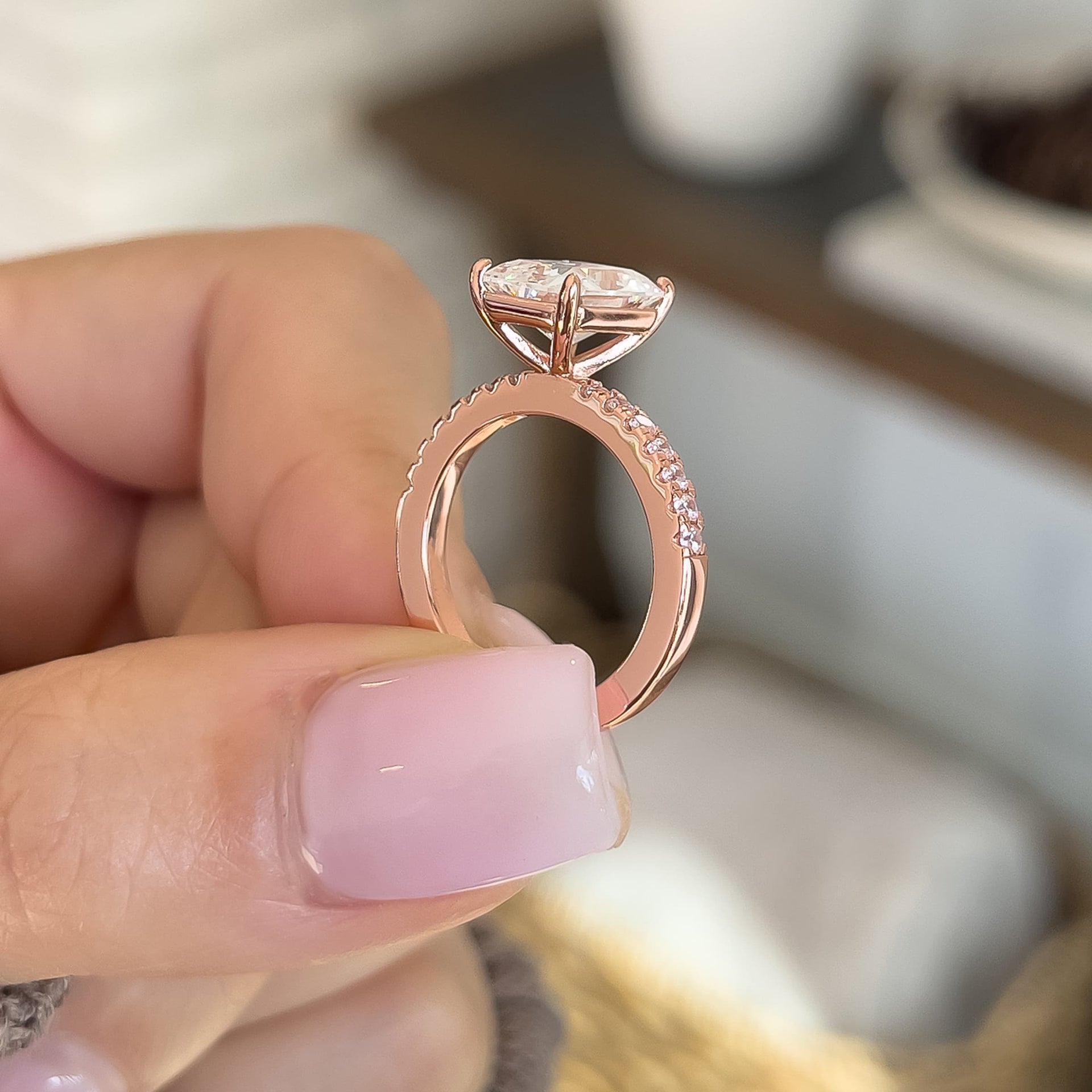 Side profile of rose gold radiant cut engagement ring with half eternity band detailing with a neutral toned background