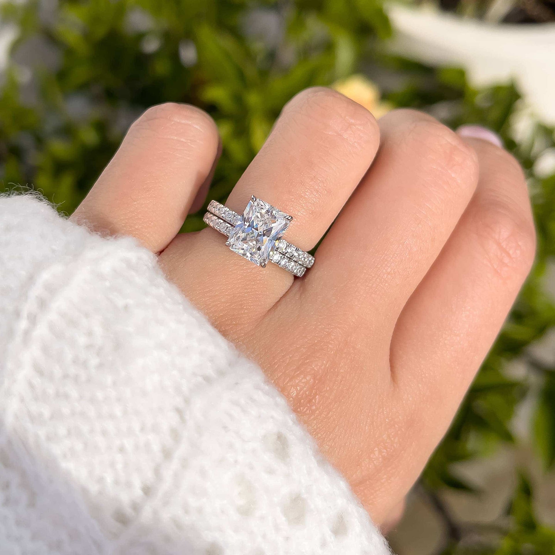 3 carat engagement ring shown in silver paired with a complementary silver wedding band shown on model with light pink nails and white sweater 