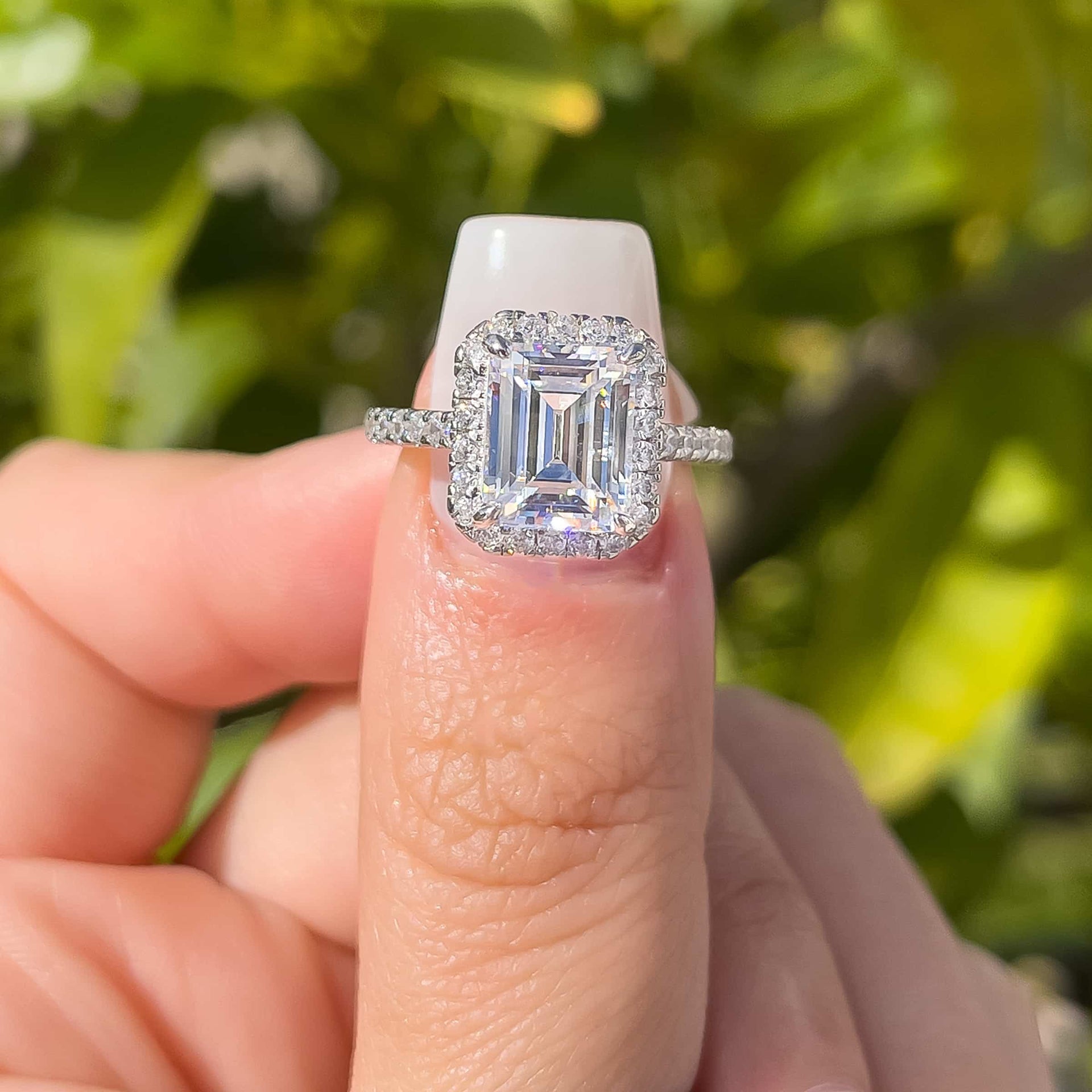 3 carat engagement ring shown in silver on thumb in front of outside greenery