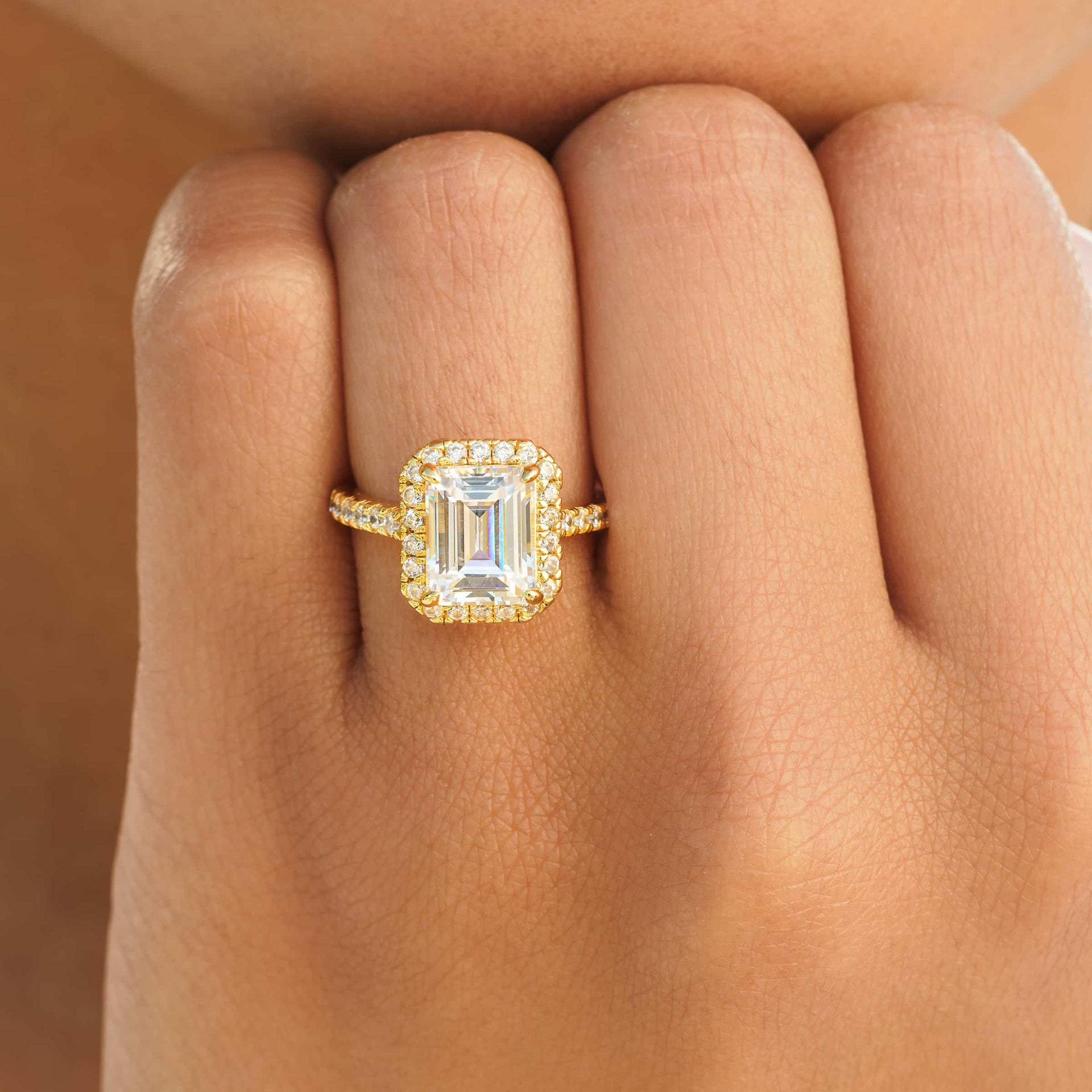 Gorgeous gold emerald cut engagement ring with halo and half eternity band detailing on female hand
