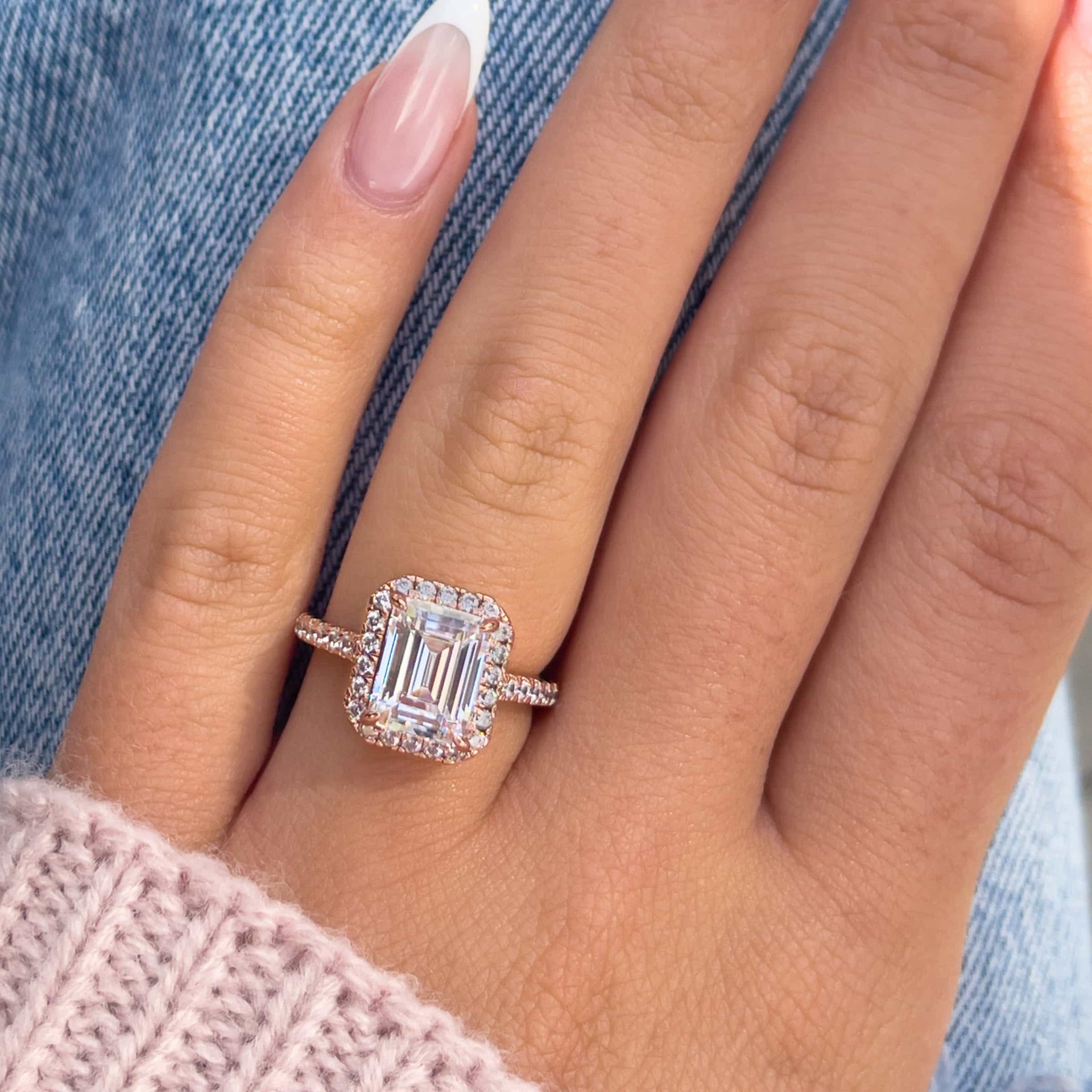 Close up on gorgeous rose gold emerald cut engagement ring modeled on hand resting on denim