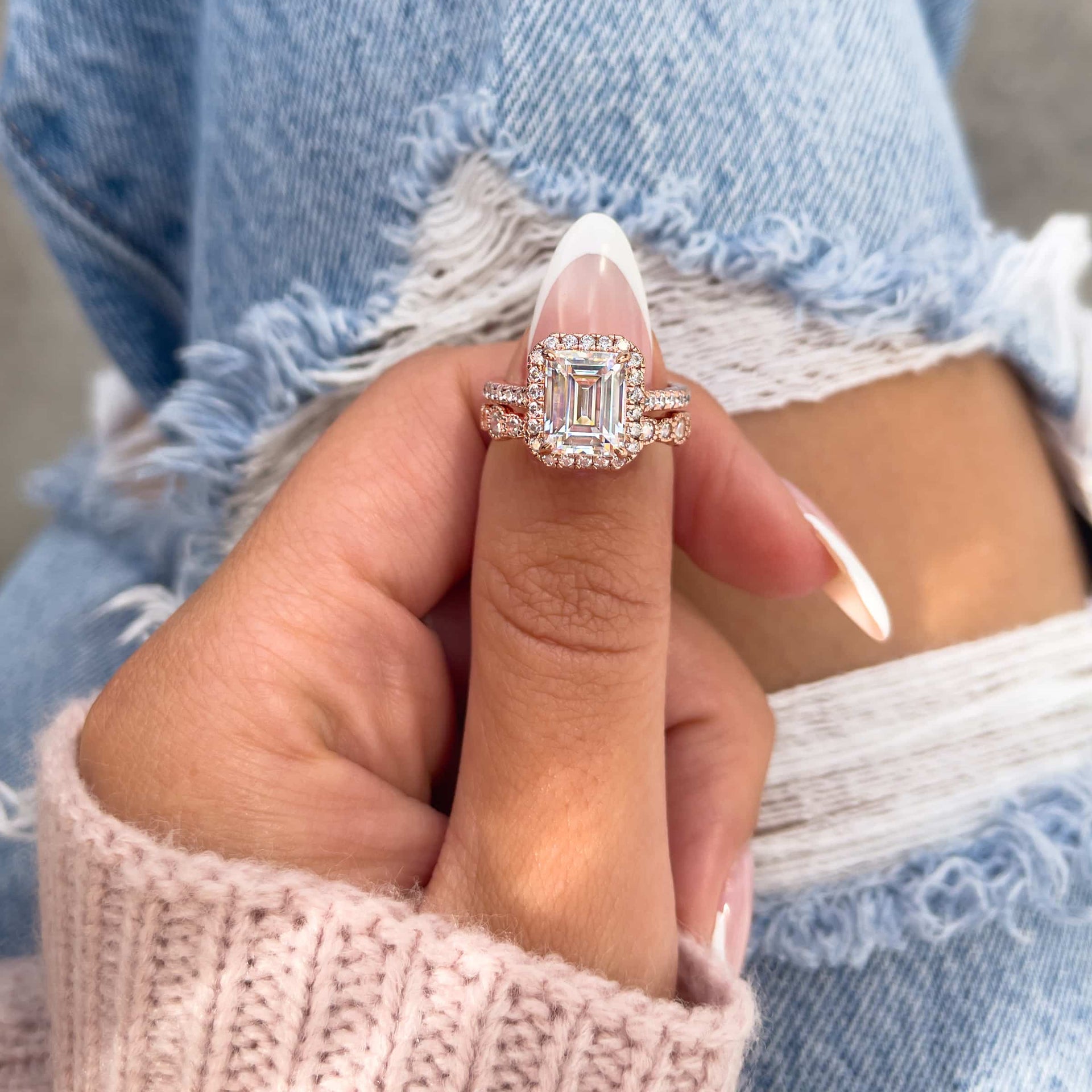 3 carat rose gold emerald cut halo engagement ring paired with vintage rose gold wedding band on model wearing denim
