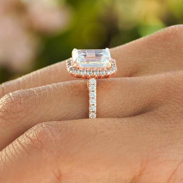 Close up side view of rose gold 3 carat engagement ring on hand in front of greenery