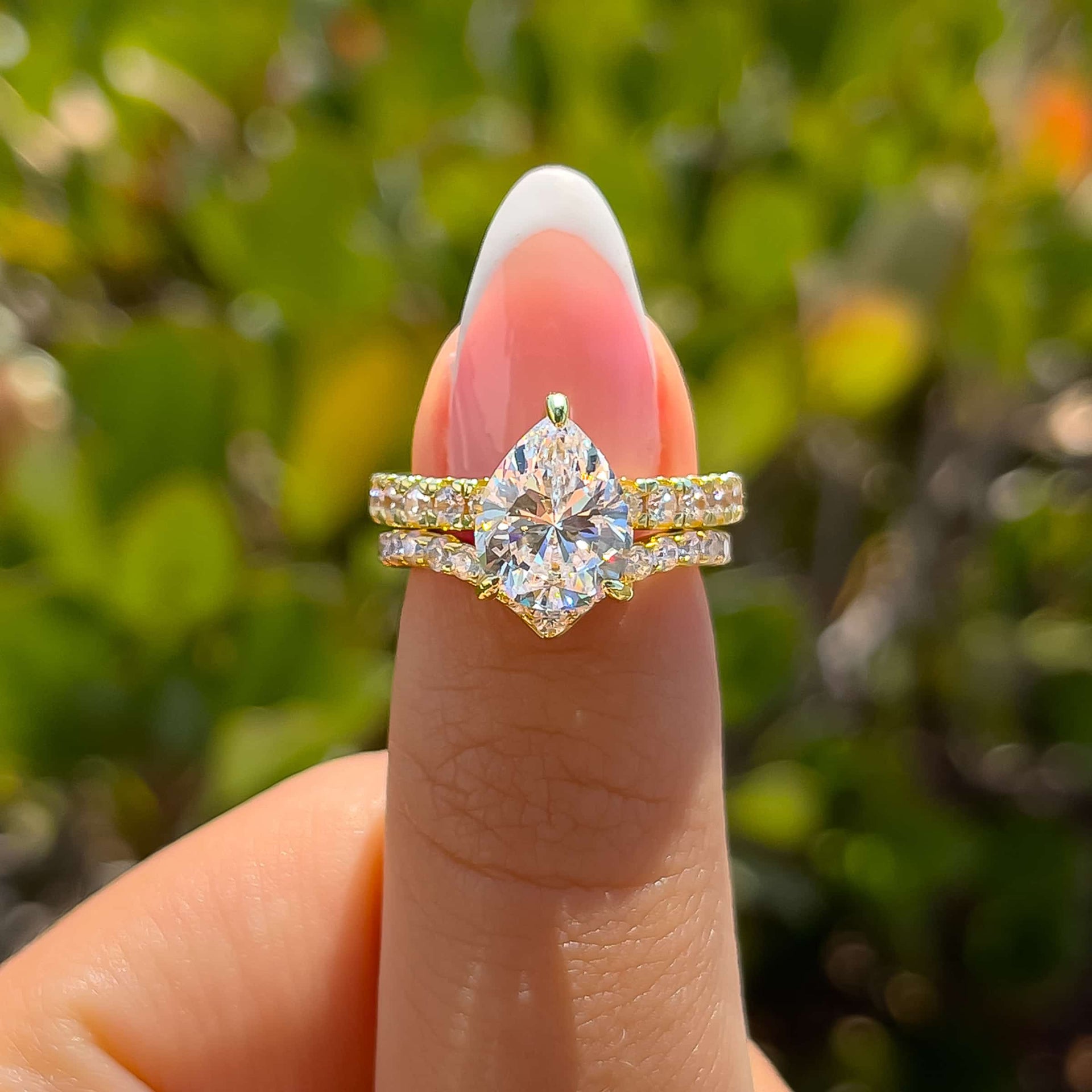 gold pear cut engagement ring paired with stunning gold chevron wedding band on model with french tip nails