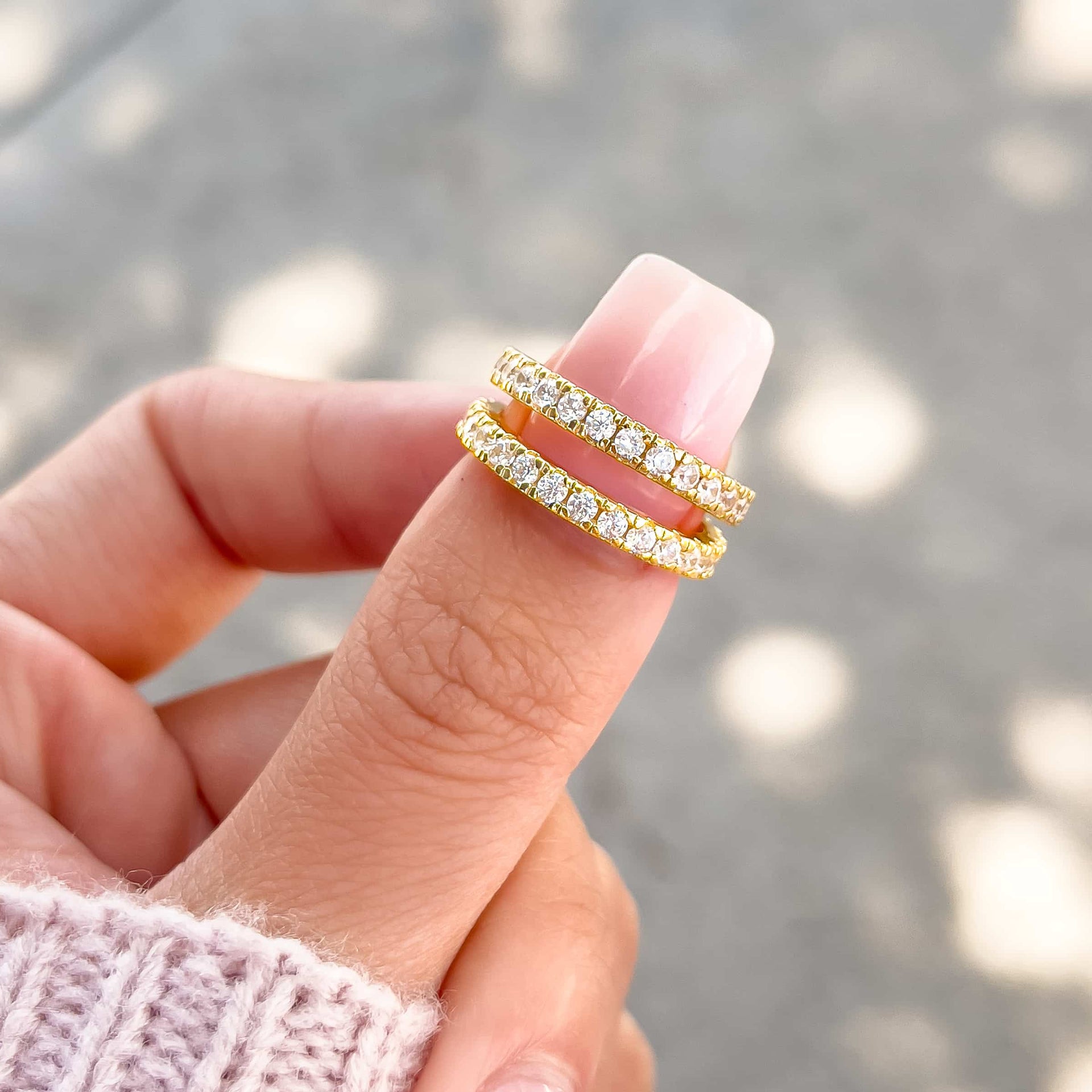 two gold statement eternity bands on female hand with neutral nail and light pink sweater