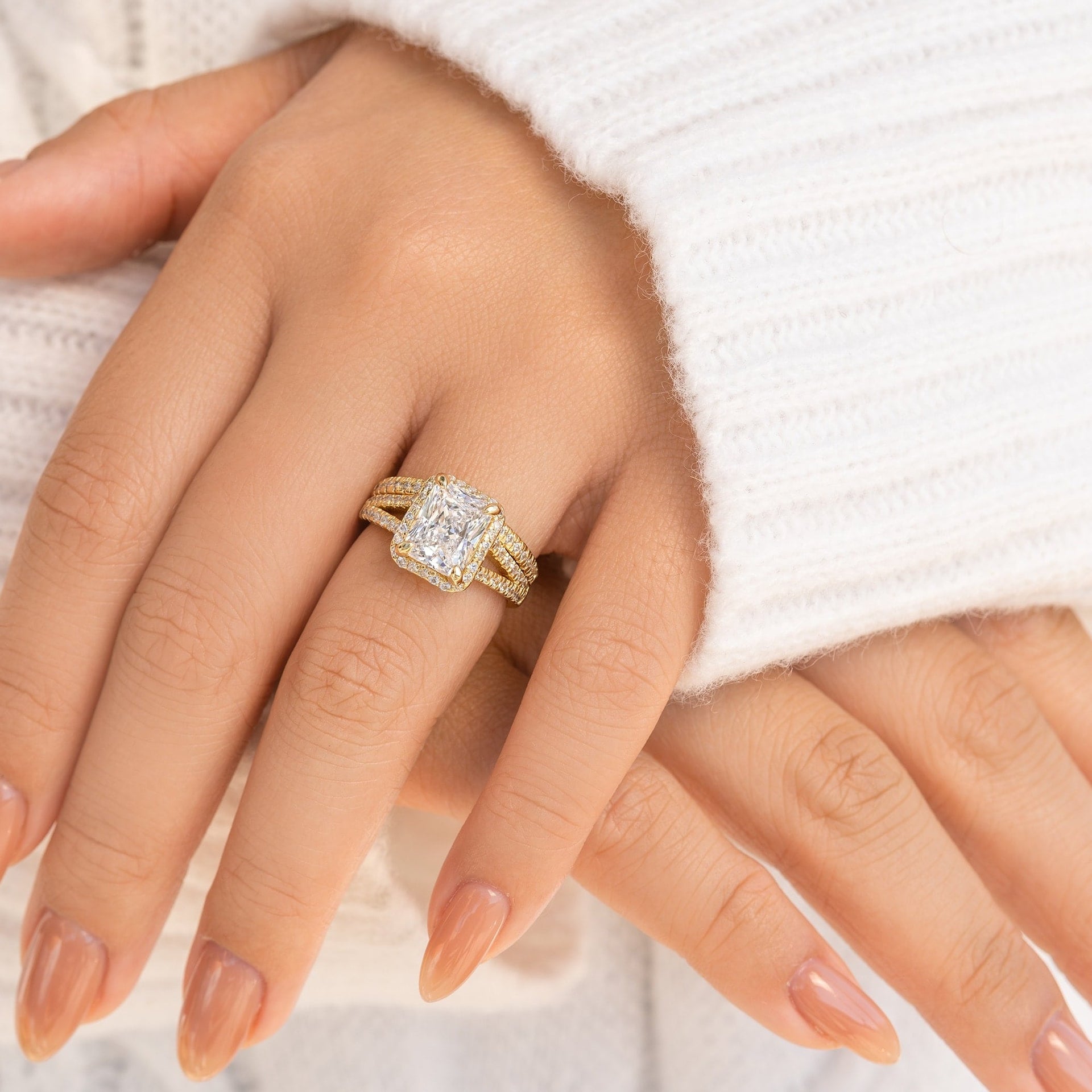 radiant gold split shank engagement ring with half eternity band modeled on female hand in white sweater