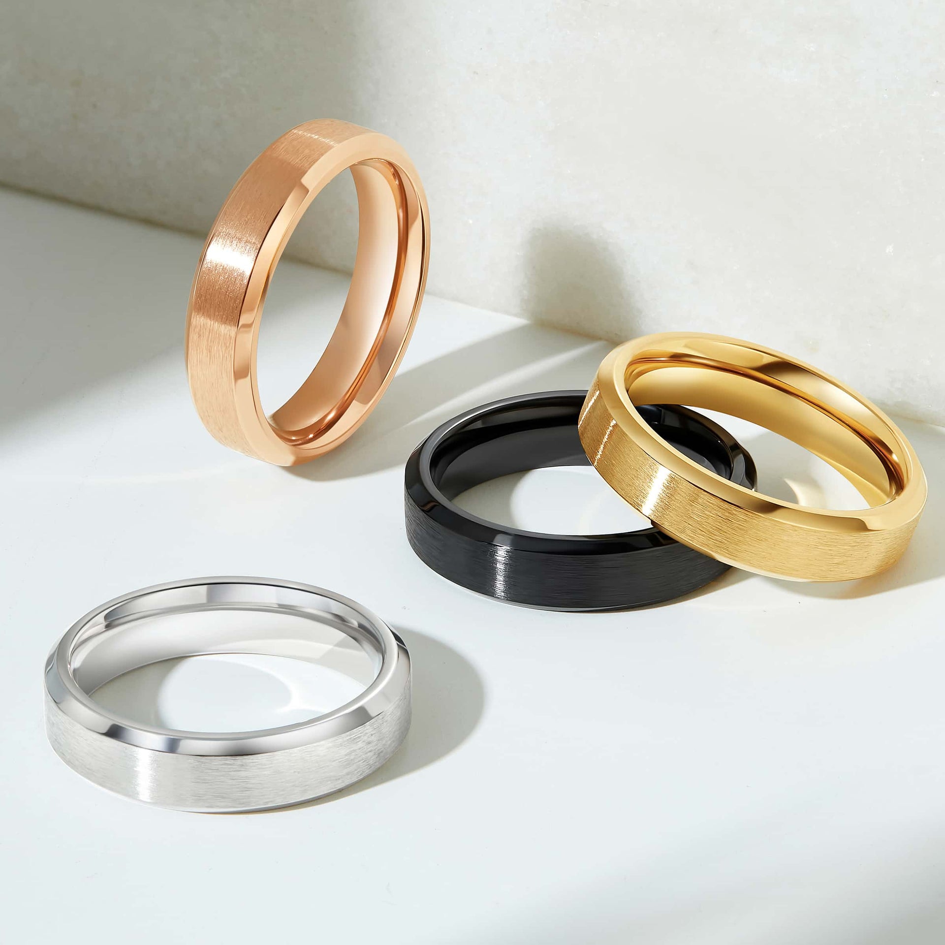 flatlay showcasing rose gold, gold, black, and silver sleek wedding bands on neutral gray background