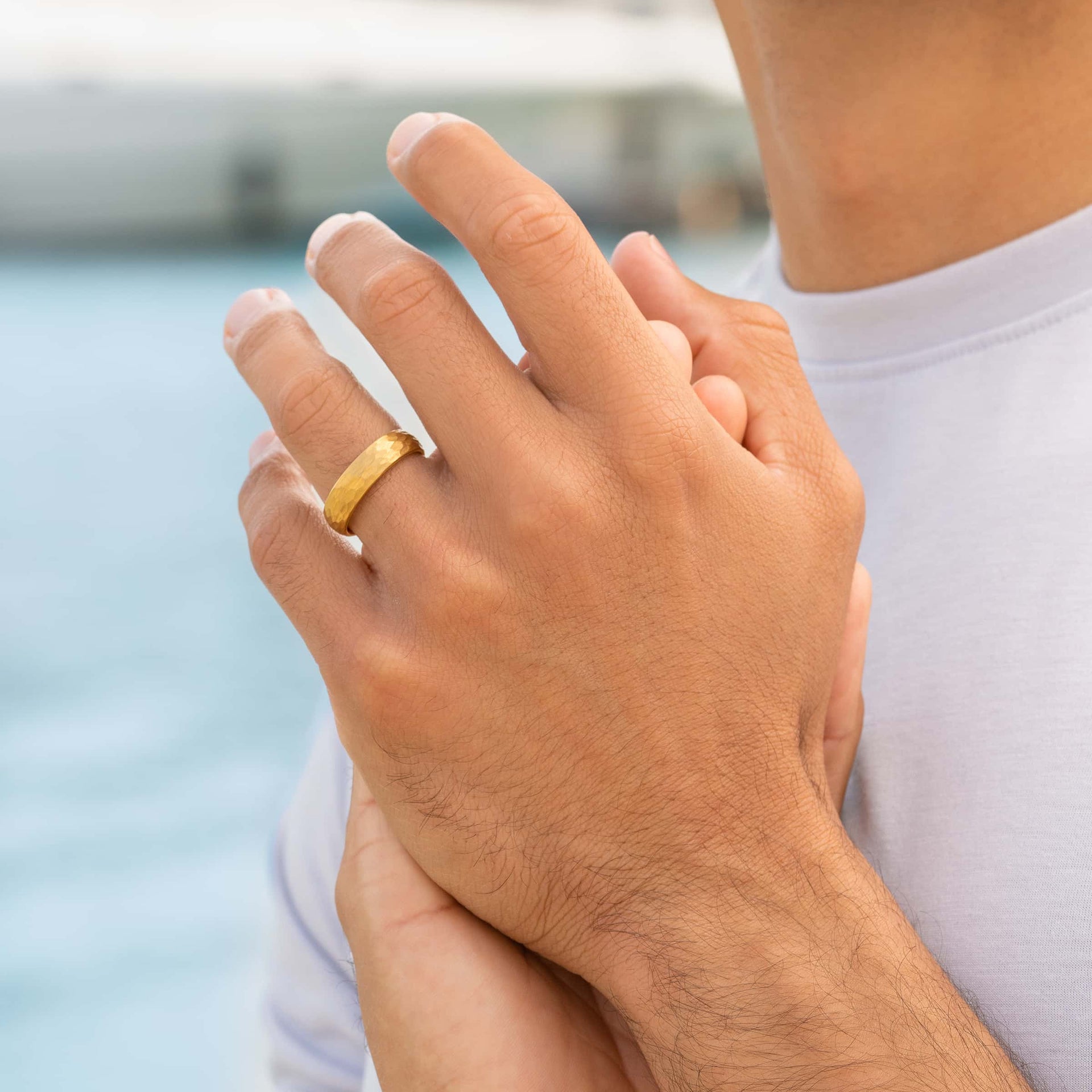 man wearing gold hammer wedding band with blue water in background