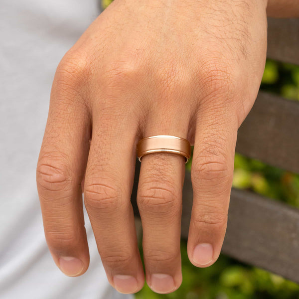 rose gold wedding band on hand with greenery in background