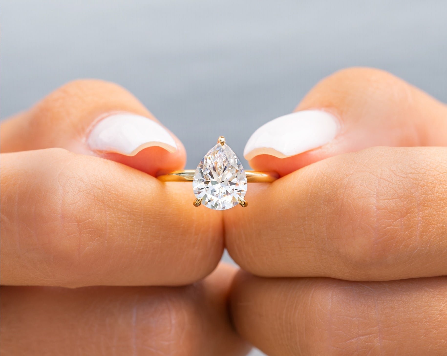 woman pinching gold pear shaped engagement ring