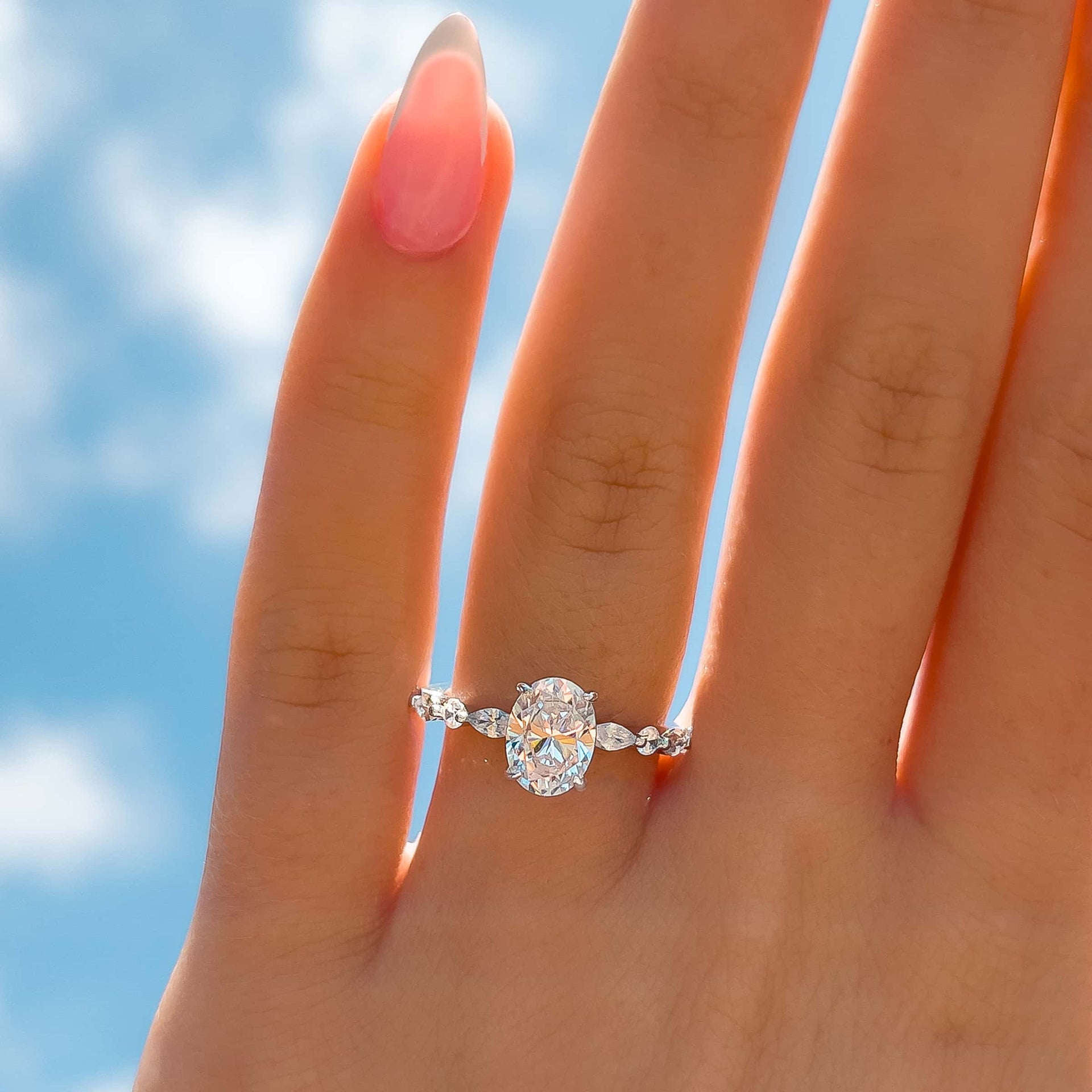 gorgeous 1.5 ct oval cut engagement ring shown in silver with blue sky in the background on female hand