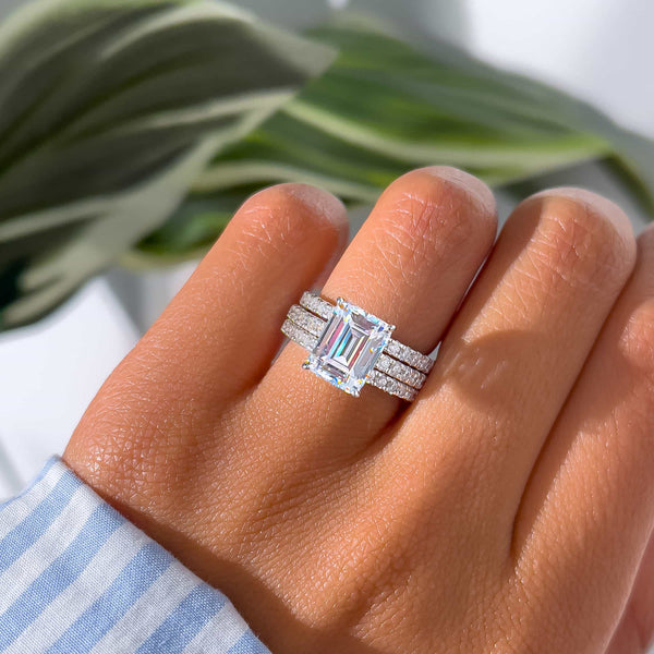 woman wearing gorgeous wedding ring stack with emerald cut engagement ring