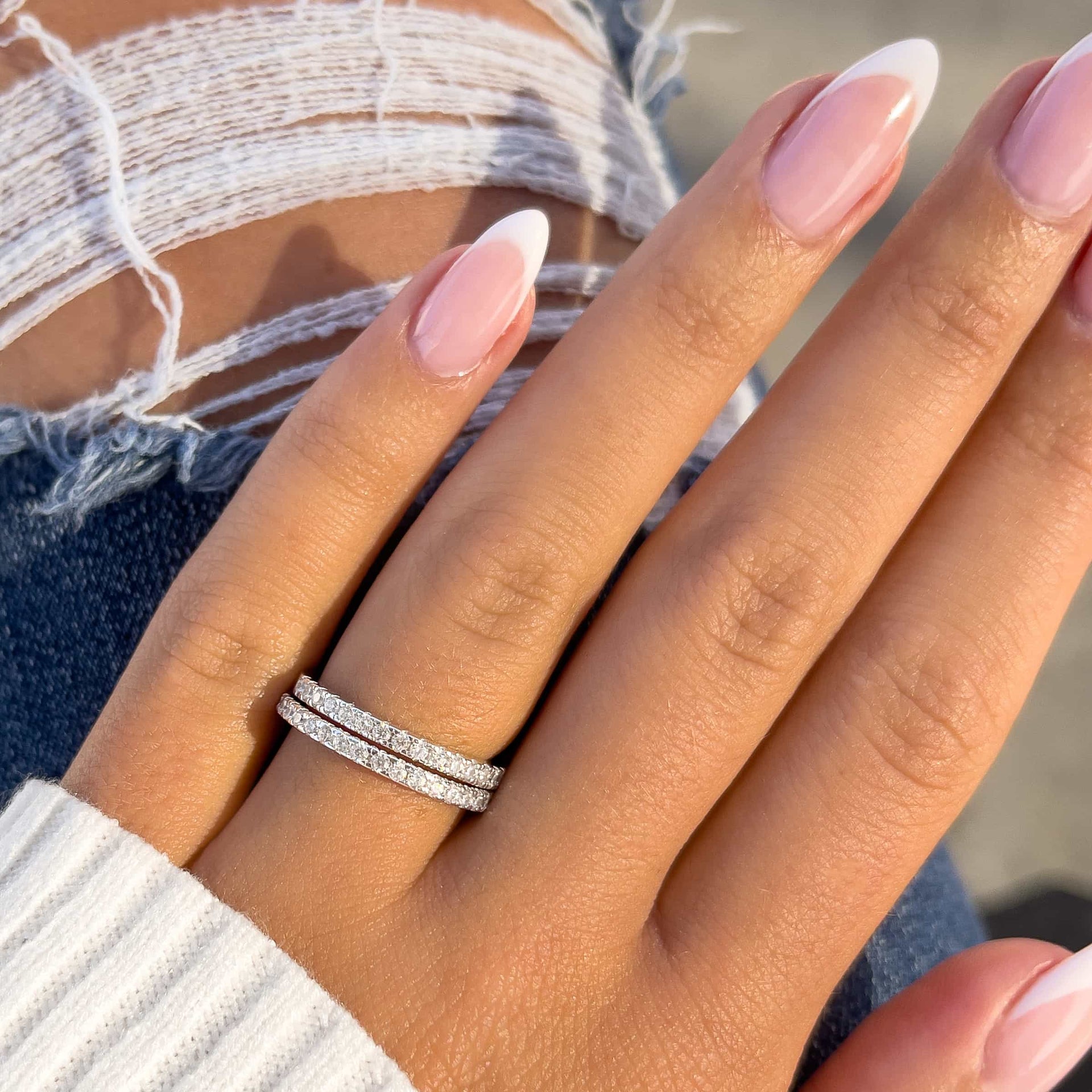 two wedding bands stacked on ladies finger with jeans and white sweater