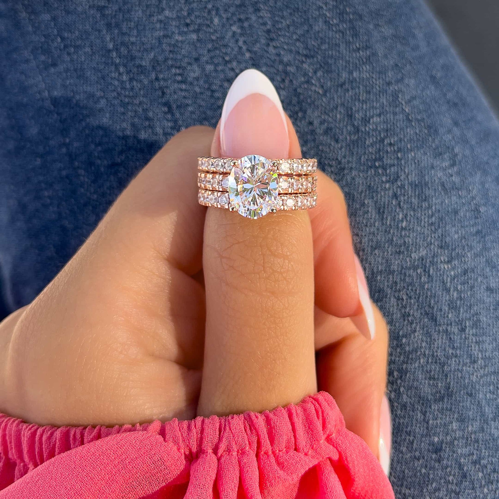 gorgeous rose gold oval triple wedding ring stack on model with french tip nails, pink top, and dark blue denim