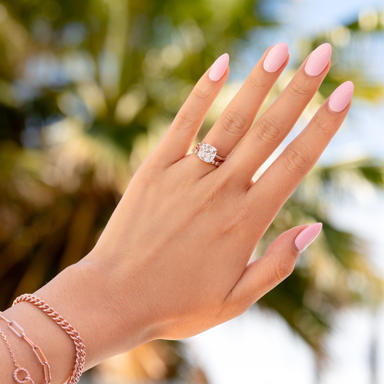 woman holding hand up to palm tree with rose gold cusion cut engagement ring