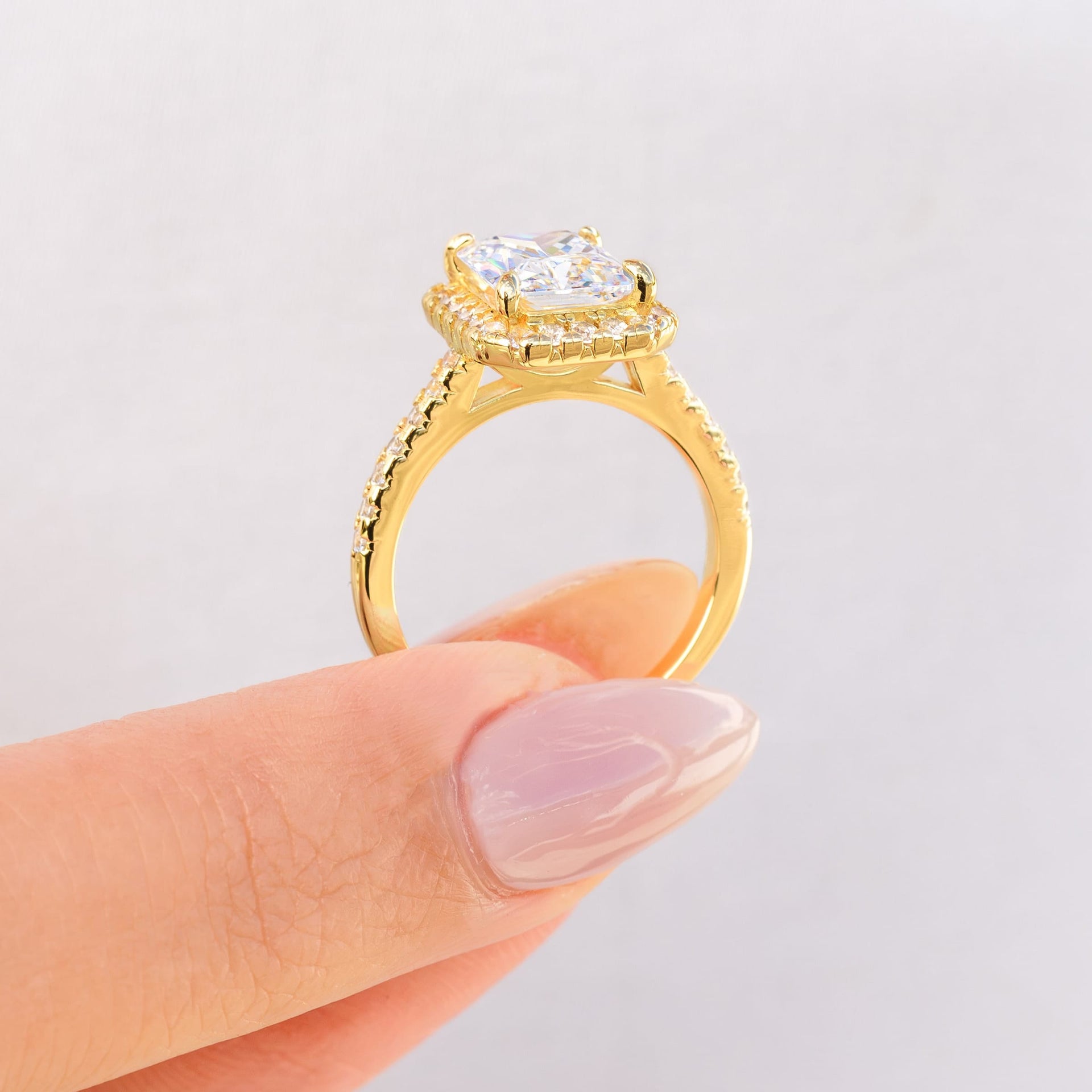 woman pinching gold engagement ring setting with halo