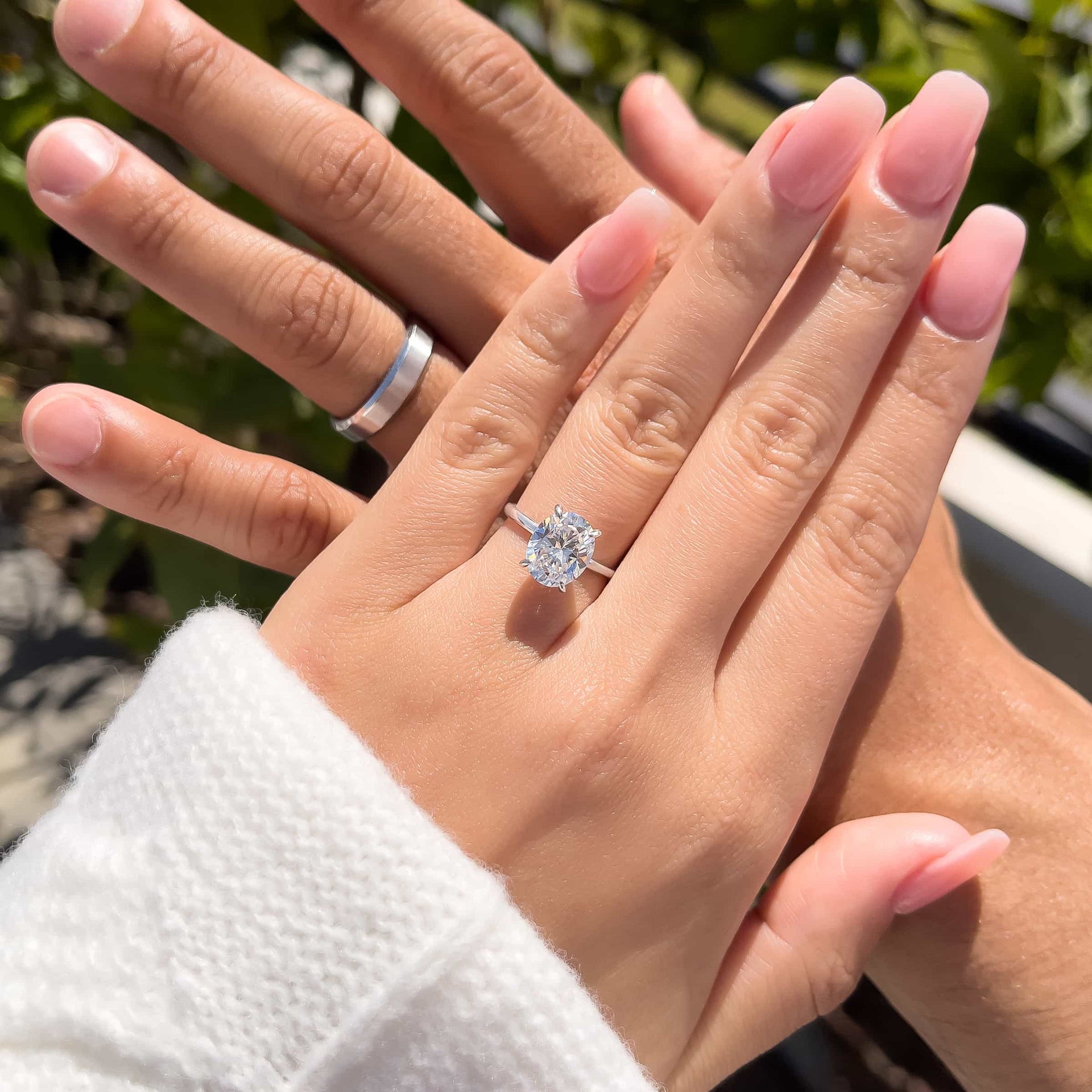 couple wearing oval engagement ring with infinity silver wedding band