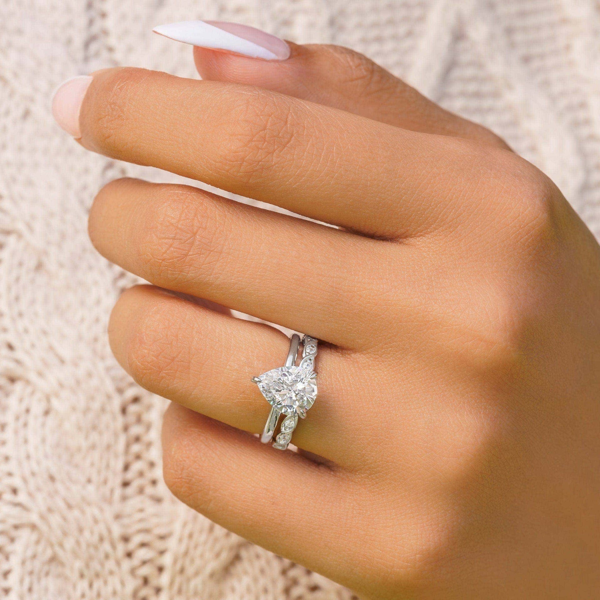 woman wearing pear shaped cut engagement ring with silver wedding band
