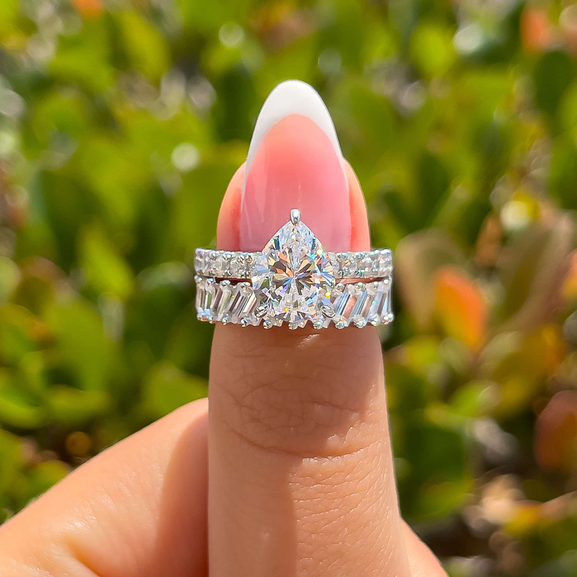 bold silver pear cut engagement ring paired with unique silver baguette wedding band held by model with french tip nails