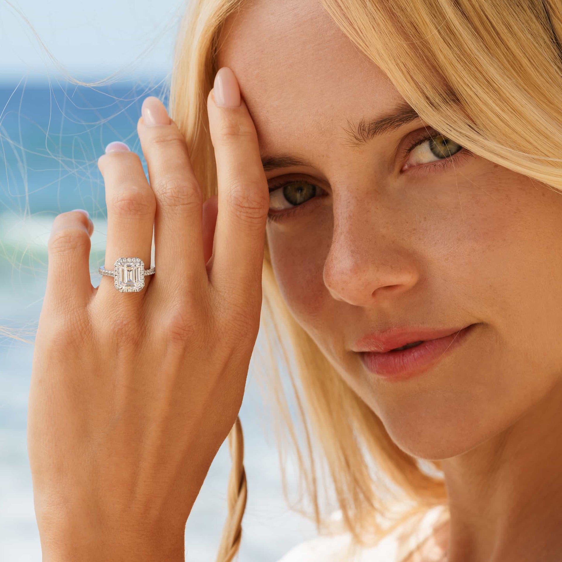 Brilliant silver emerald cut engagement ring with halo and half eternity band detailing on blonde model with neutral nails