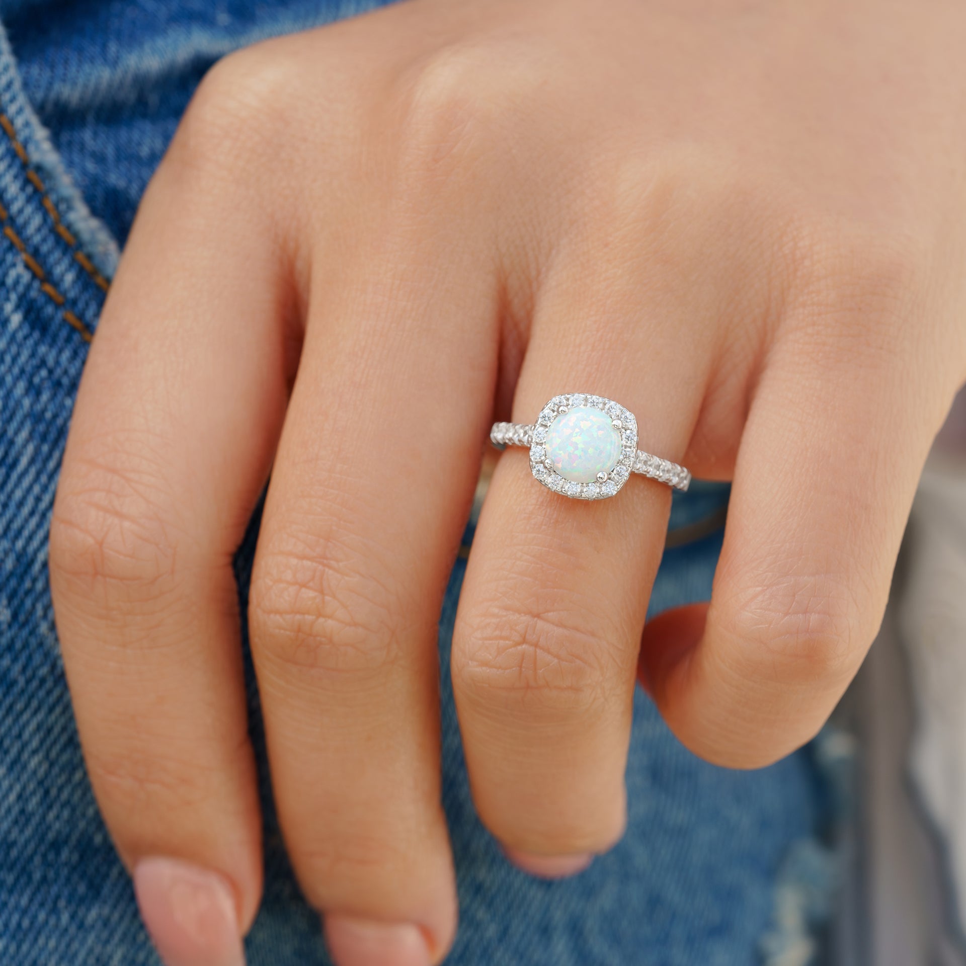 silver halo opal engagement ring on ladies hand by jeans