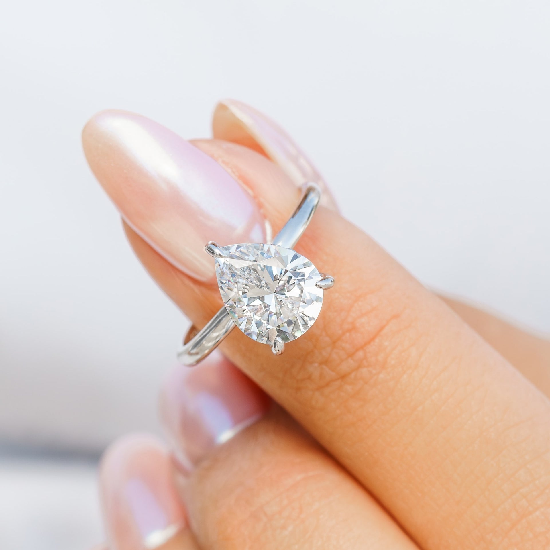woman pinching pear shaped silver engagement ring