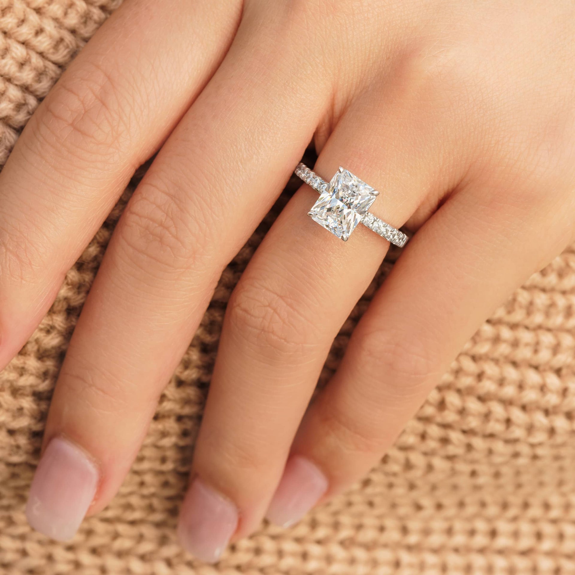 Gorgeous silver radiant cut engagement ring on female model wearing tan sweater