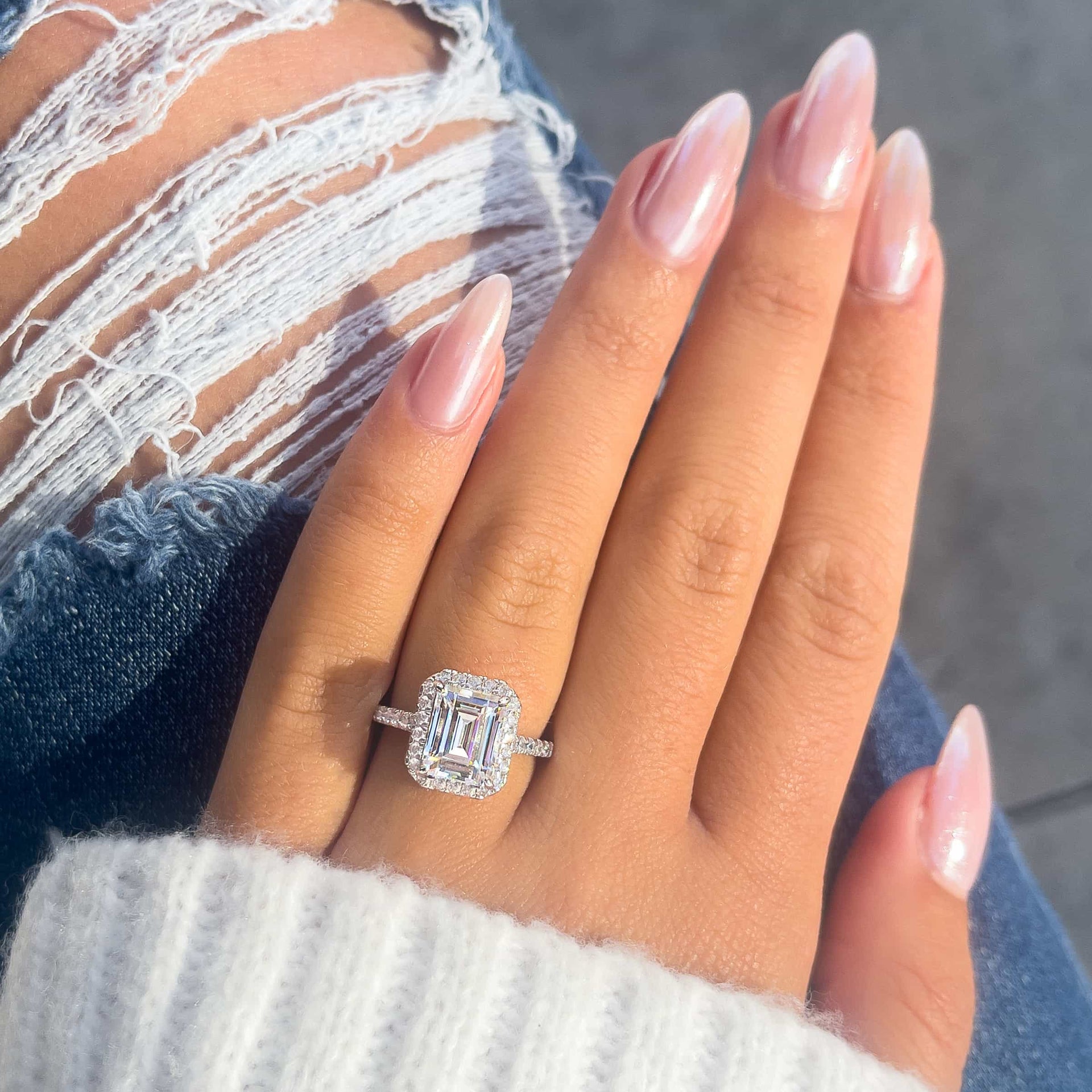 silver halo emerald cut engagement ring on ladies hand with blue jeans in background