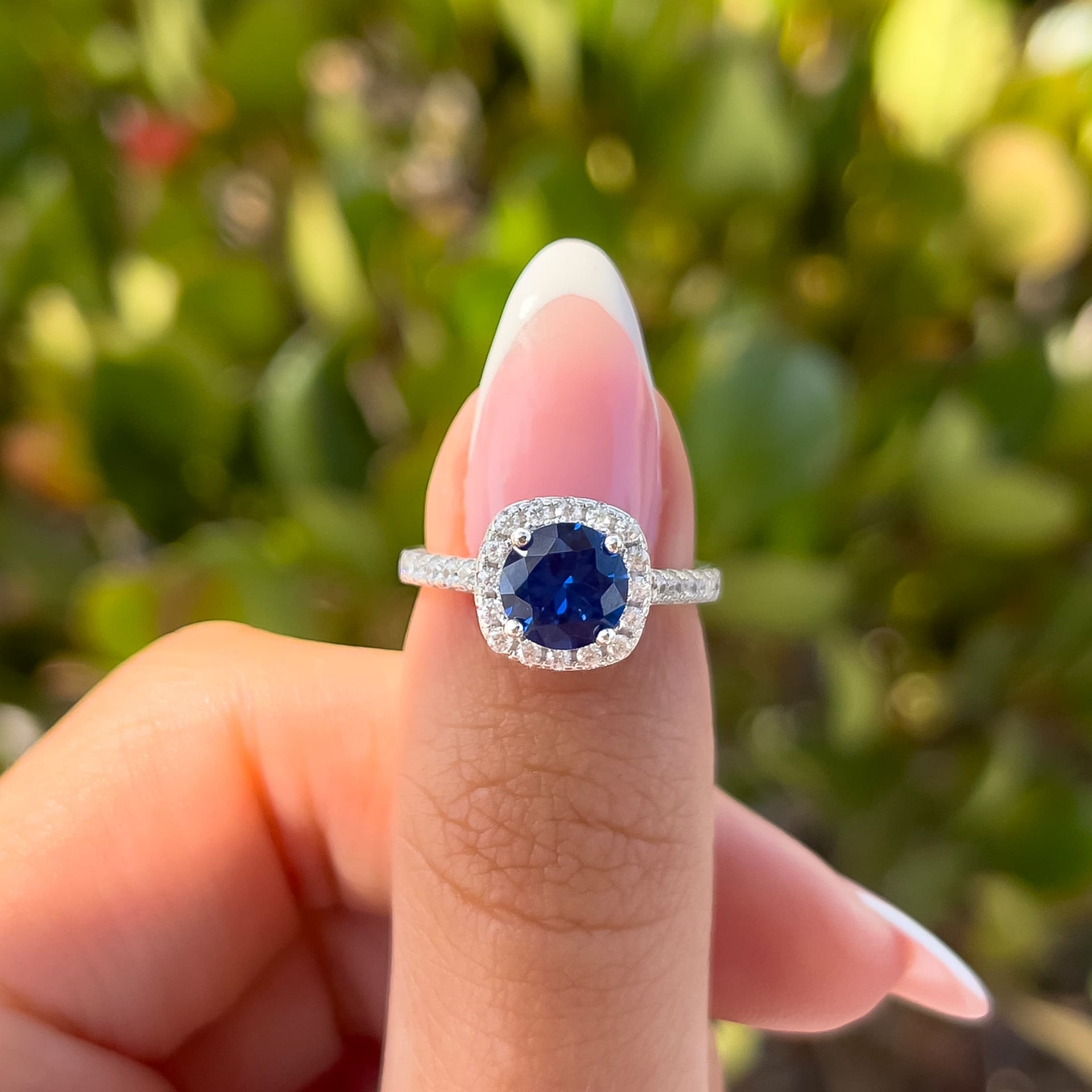 round cut halo tanzanite engagement ring with half eternity band detailing on female hand with french tip nails