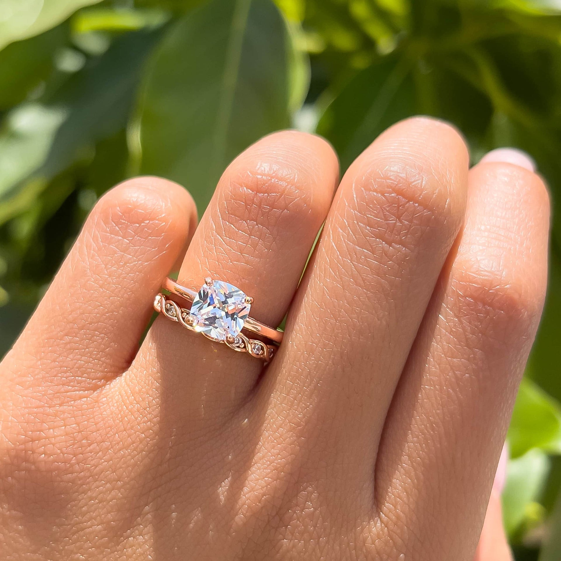 Rose gold 1 carat cushion cut solitaire engagement ring on female hand in front of greenery