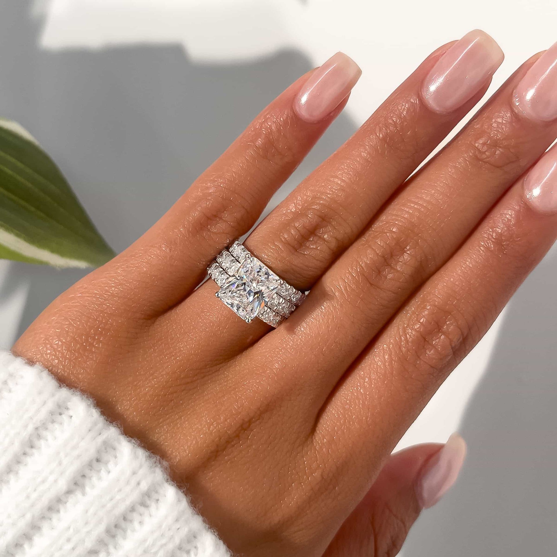 set of two eternity bands modeled with radiant cut engagement ring on female hand with neutral nails and white sweater