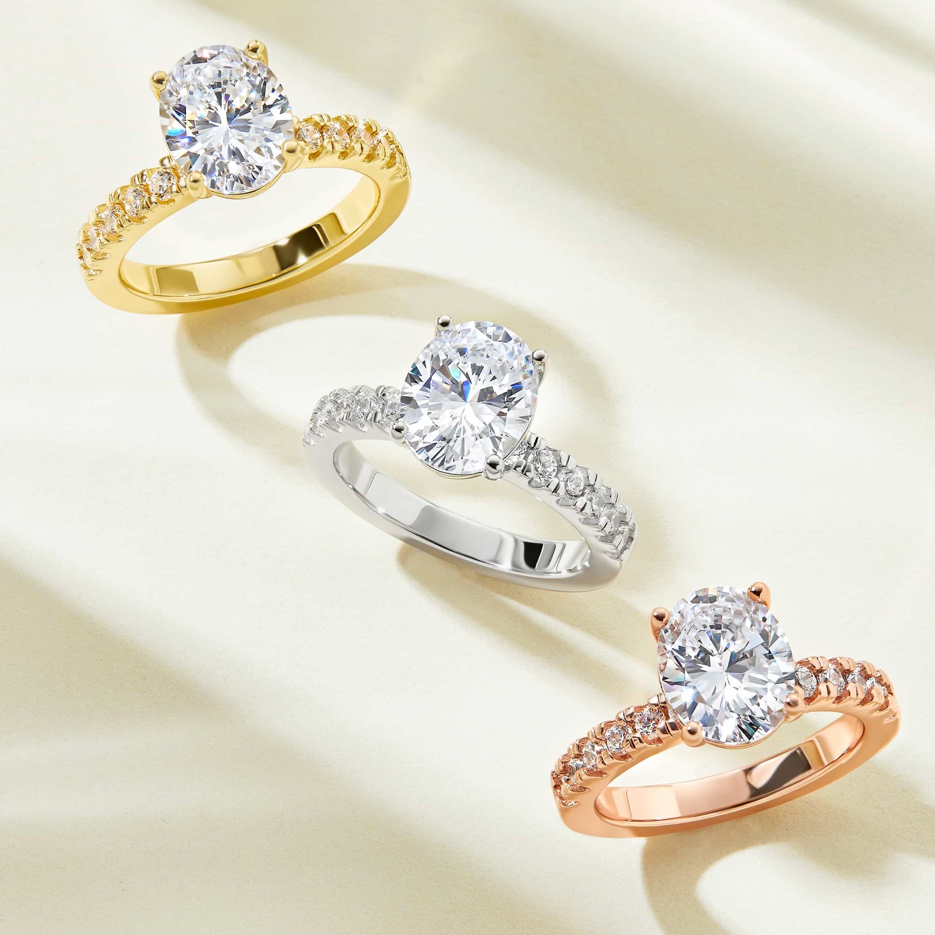 a gold, silver, and rose gold versions of a 3 carat oval cut engagement ring with a thick eternity band detailing