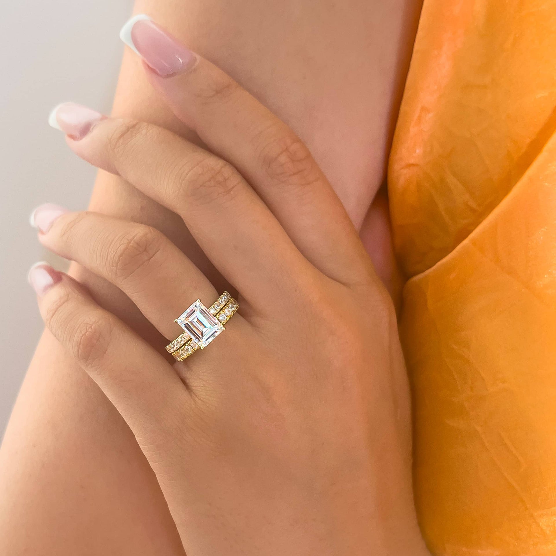 gorgeous gold emerald cut engagement ring with matching gold wedding band on model with orange top and french tip nails