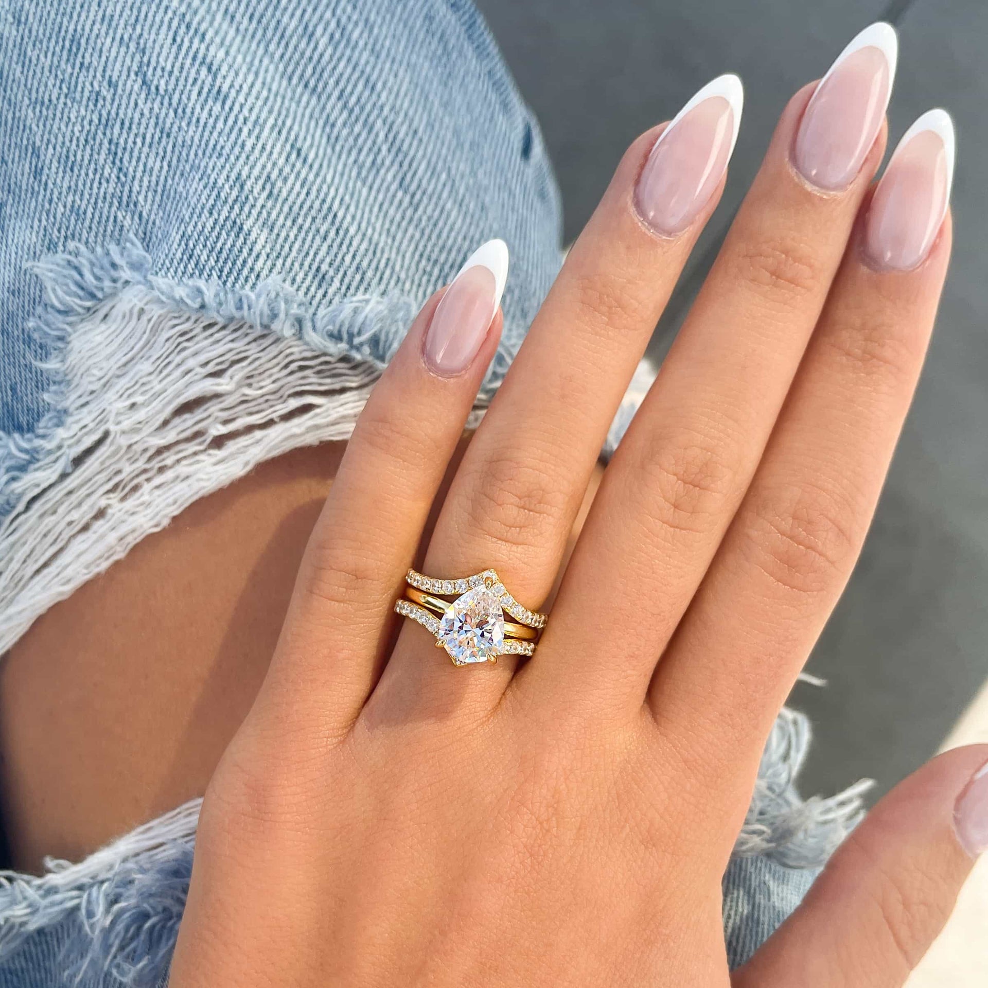 Two gold v-shaped half eternity wedding bands paired with a gold pear cut solitaire engagement ring modeled on female hand with French tip nails