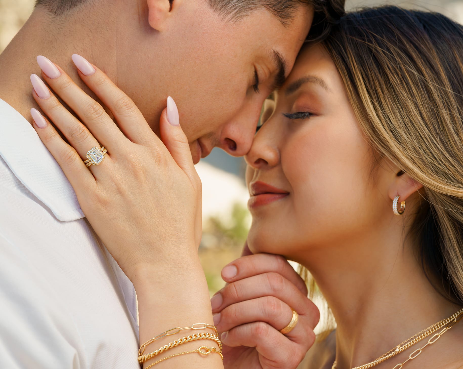couple wearing gold emerald cut engagement ring with gold mens wedding band and gold accessories