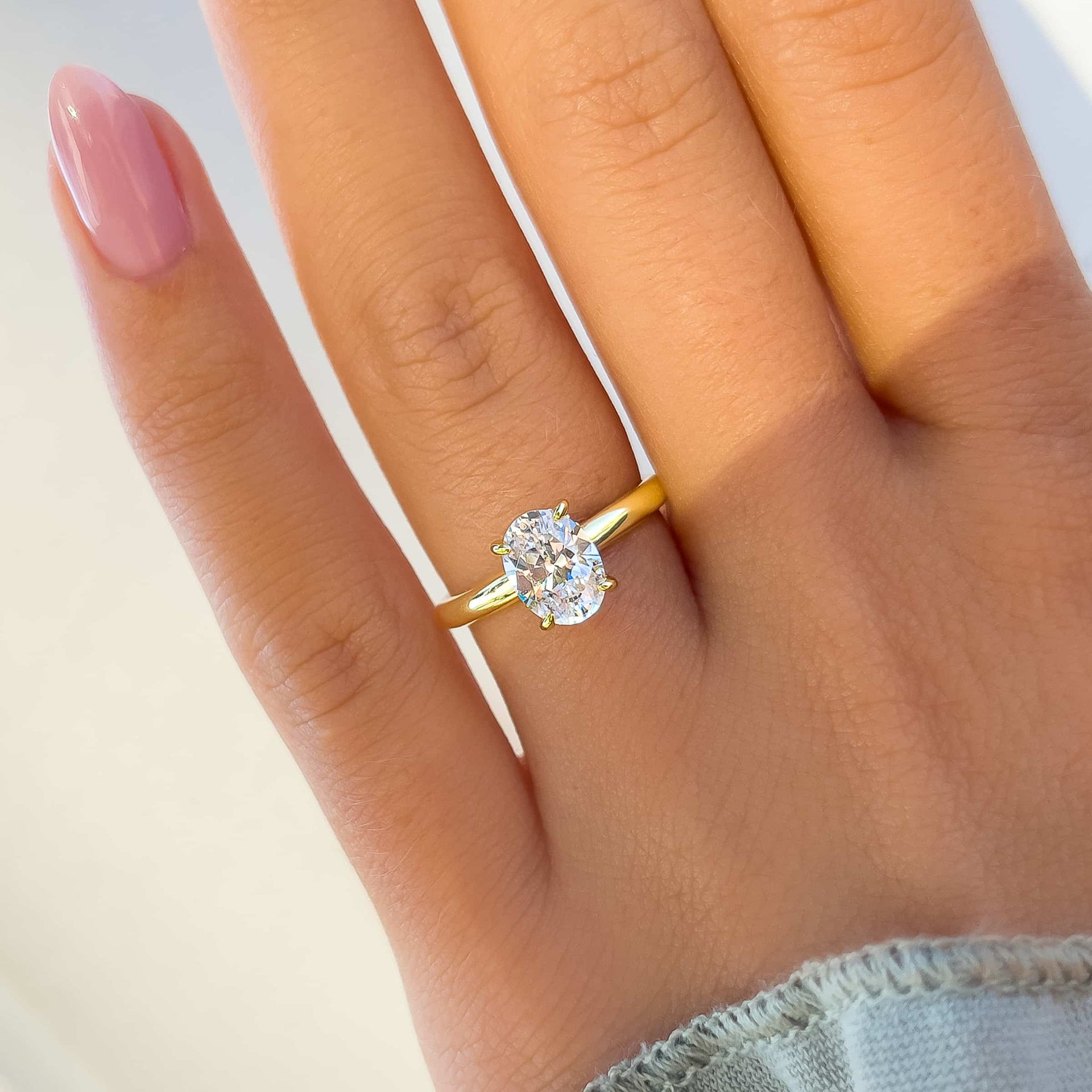 beautiful gold solitaire engagement ring with shining oval stone on model with pink nails and green shirt